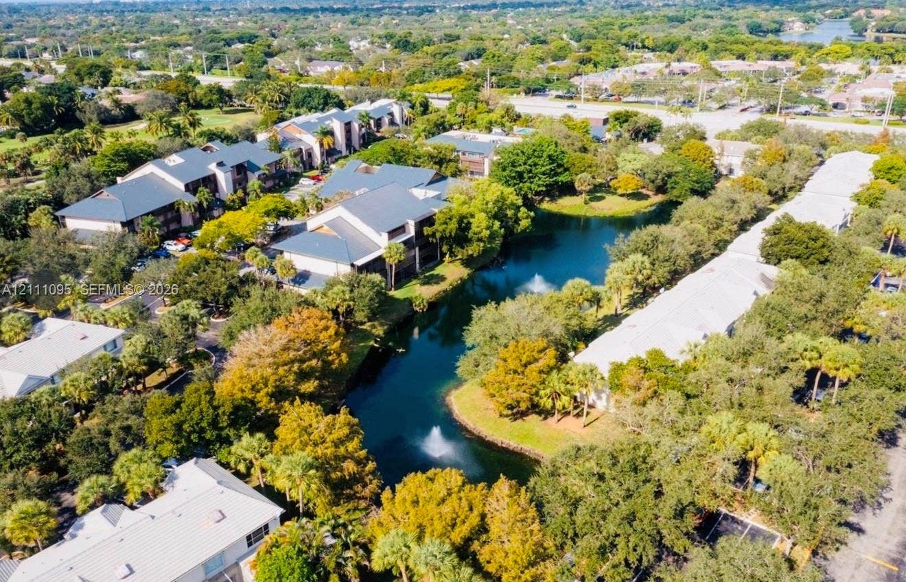 120 SW 96th Terrace, #104, Plantation, FL 33324 Aerial perspective featuring multi-story residential buildings, a central pond with a fountain feature, abundant mature canopy trees, and paved surface parking