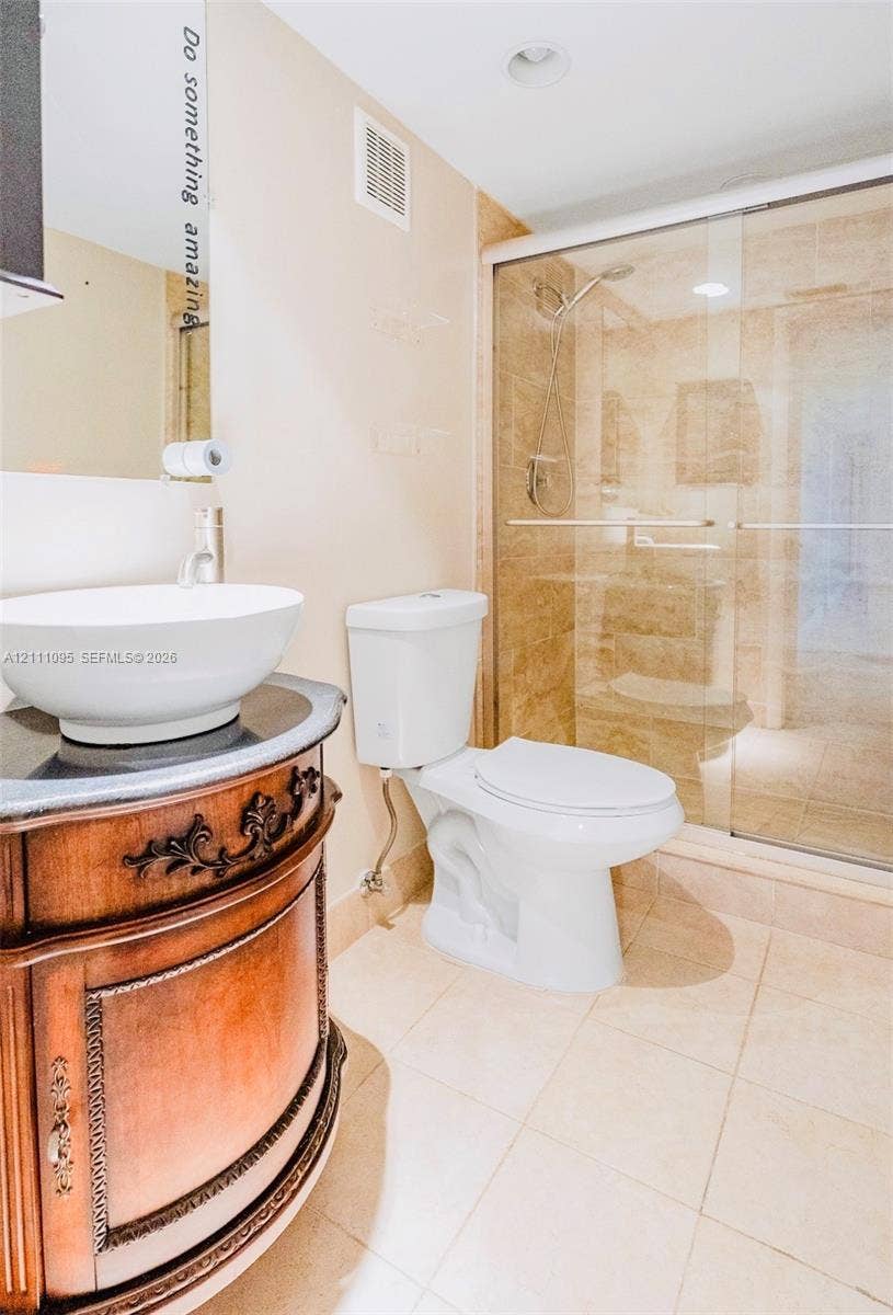 120 SW 96th Terrace, #104, Plantation, FL 33324 Bathroom featuring an ornate wooden vanity with a stone countertop, white vessel sink, glass-enclosed shower with tile surround, and tiled flooring