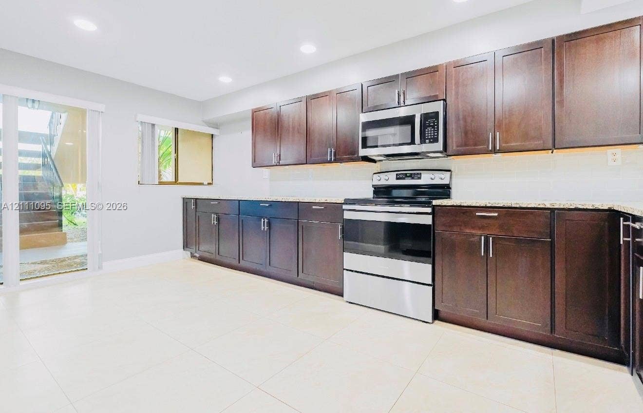 120 SW 96th Terrace, #104, Plantation, FL 33324 Kitchen featuring dark wood-finish cabinetry, stainless steel appliances, stone-look countertops, recessed lighting, and large-format tile flooring