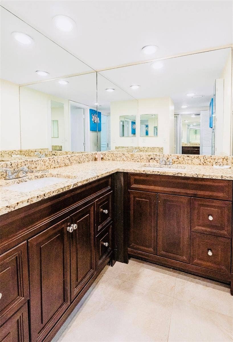 120 SW 96th Terrace, #104, Plantation, FL 33324 Double vanity featuring dark wood-finish cabinetry, stone-texture countertops with dual undermount sinks, and a large-format wall-to-wall mirror with integrated recessed lighting