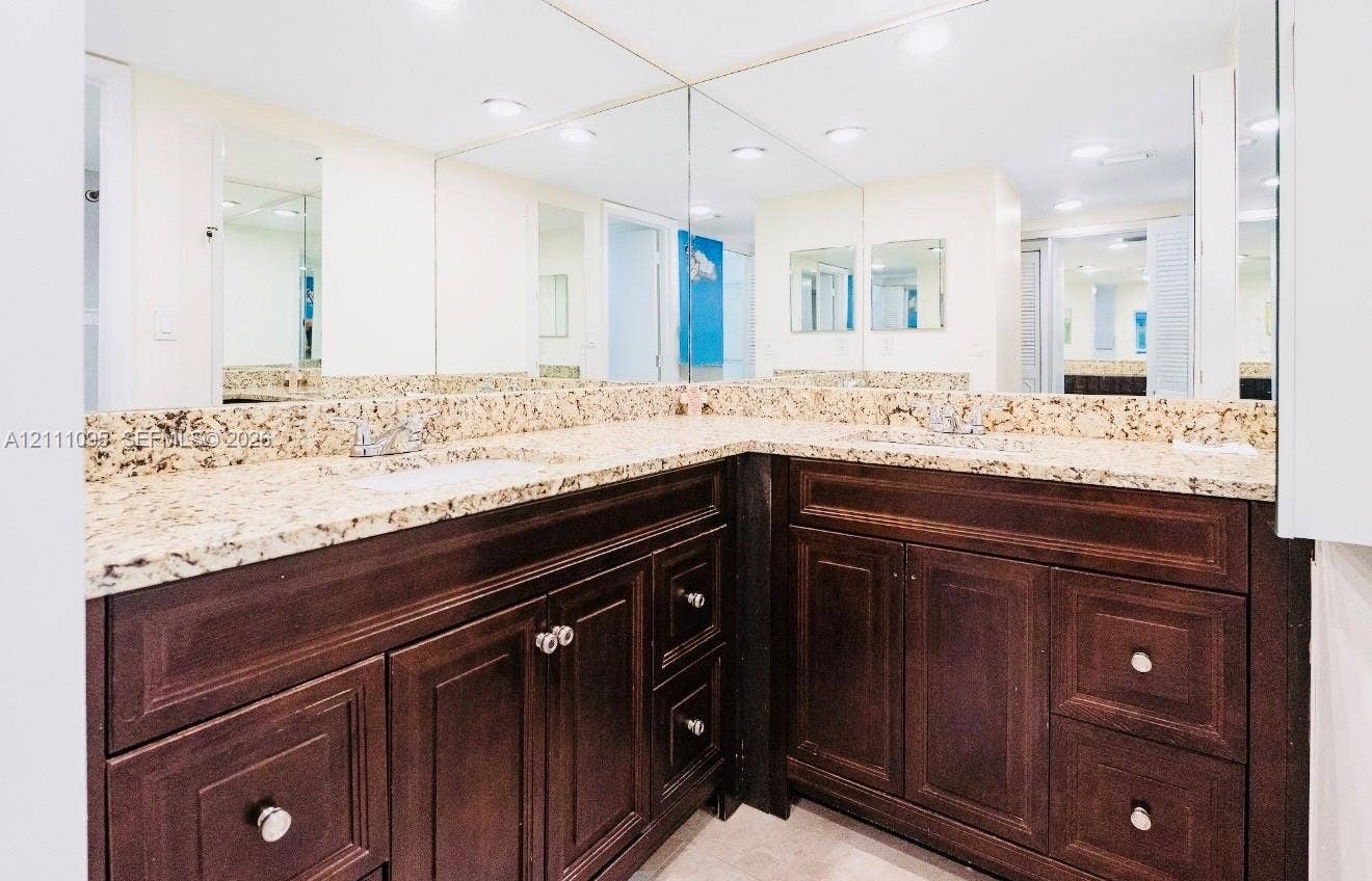 120 SW 96th Terrace, #104, Plantation, FL 33324 L-shaped vanity featuring dark wood-finish cabinetry, a stone-composite countertop, dual undermount sinks with metal hardware, and an expansive wall-to-wall mirror