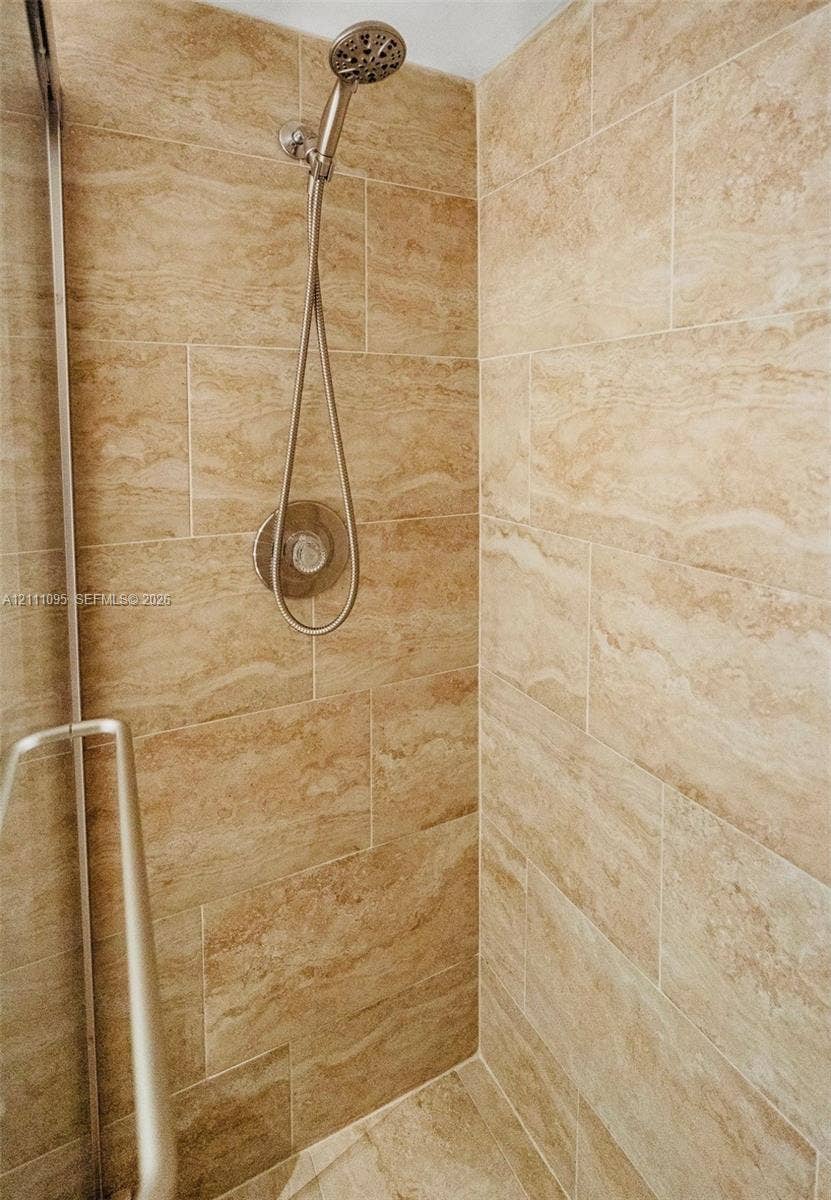 120 SW 96th Terrace, #104, Plantation, FL 33324 Shower enclosure featuring floor-to-ceiling stone-finish tile, adjustable handheld shower fixture, circular polished metal control valve, and semi-frameless metal door hardware