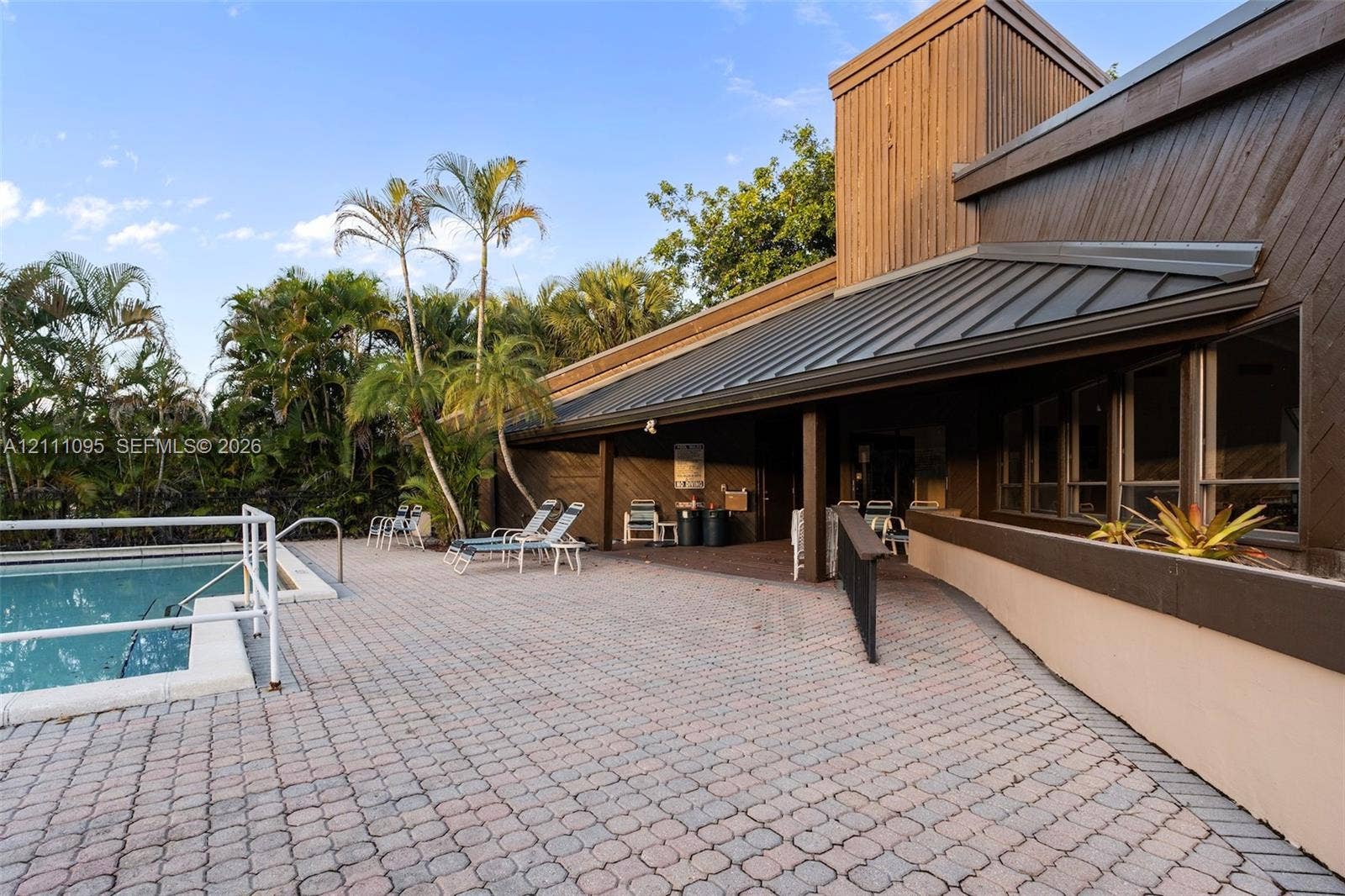 120 SW 96th Terrace, #104, Plantation, FL 33324 Outdoor pool featuring a paved deck, dark metal roofing, wood siding, and surrounding palm trees