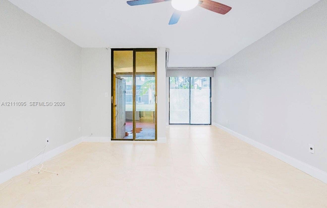 120 SW 96th Terrace, #104, Plantation, FL 33324 Neutral-toned interior featuring large-format tile flooring, dual sliding glass doors, and a ceiling fan with integrated lighting