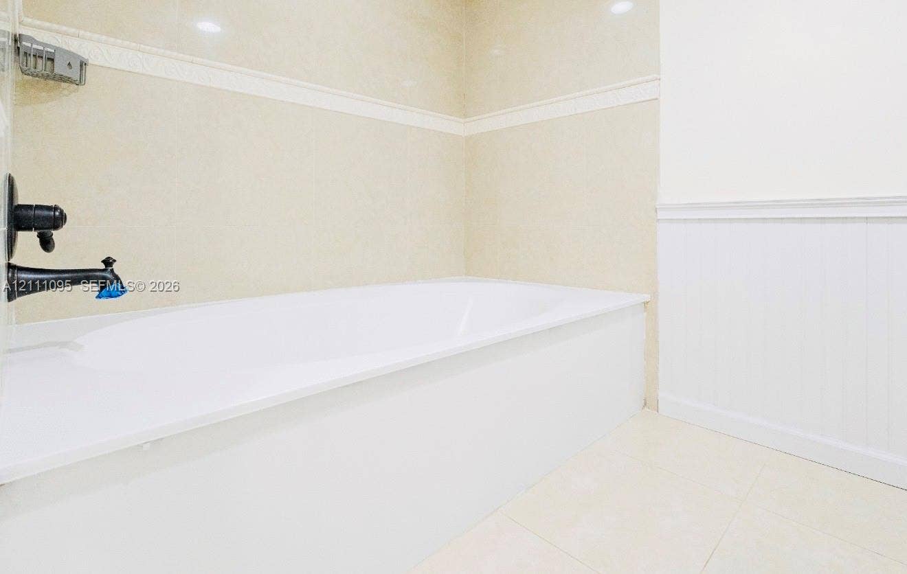 120 SW 96th Terrace, #104, Plantation, FL 33324 Built-in soaking tub with a wall-mounted matte black faucet, ceramic wall tile surround, integrated metal soap dish, and white wainscoting