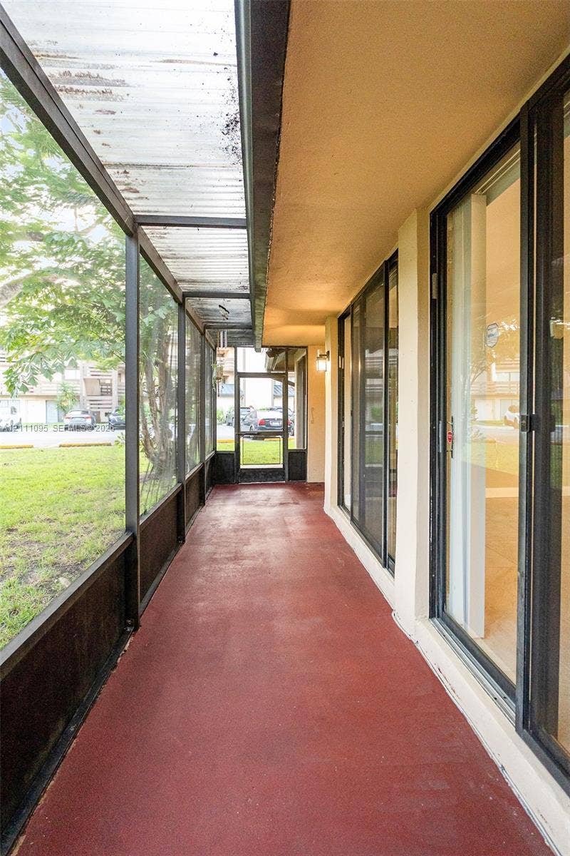 120 SW 96th Terrace, #104, Plantation, FL 33324 Enclosed exterior porch featuring dark metal screening, a corrugated translucent roof panel, painted concrete flooring, and sliding glass entry doors