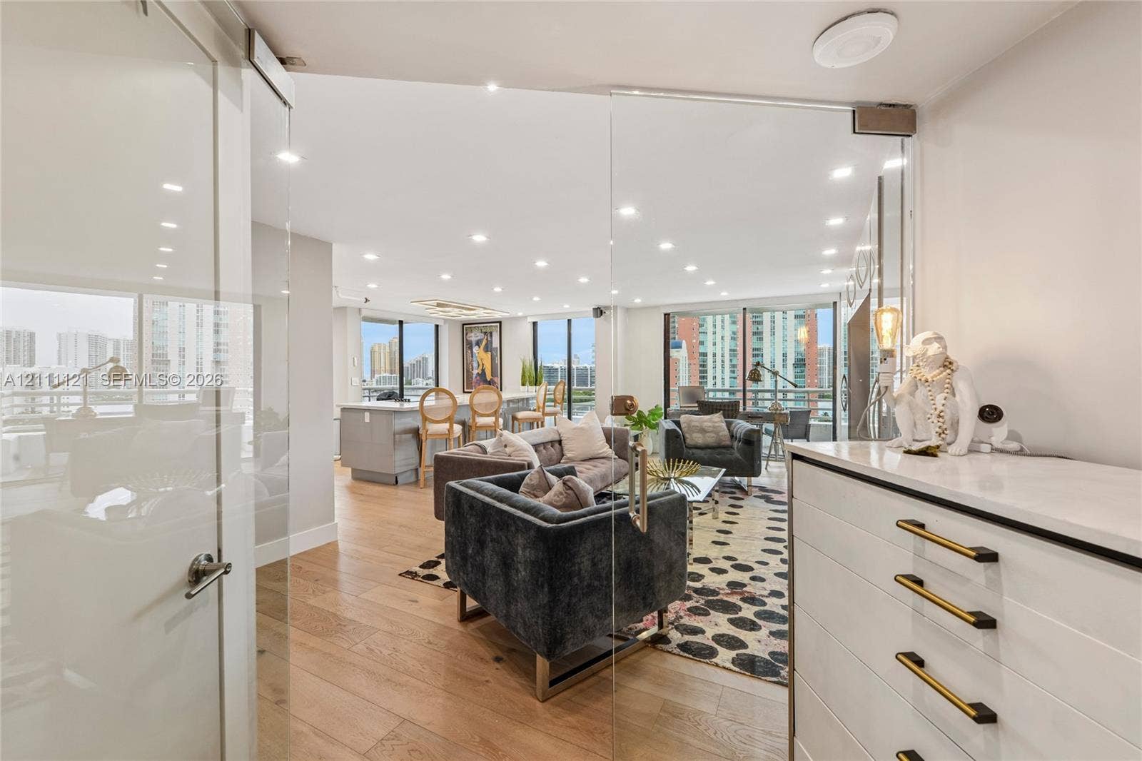 3300 NE 192nd Street, #1813, Aventura, FL 33180 Frameless glass pivot door, light-toned wood-finish flooring, recessed ceiling lighting, floor-to-ceiling windows, and built-in cabinetry with matte finish hardware