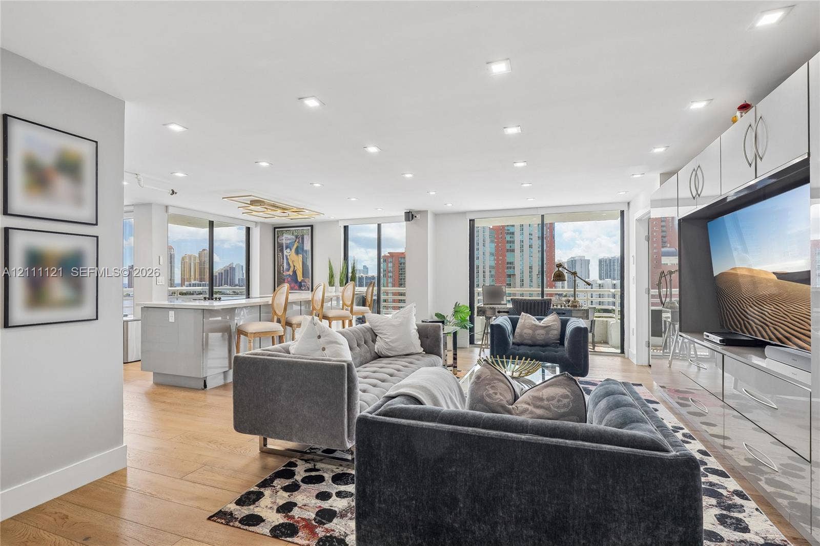 3300 NE 192nd Street, #1813, Aventura, FL 33180 Open-concept main living area featuring wood-finish flooring, recessed lighting, floor-to-ceiling glass sliding doors, and custom built-in white cabinetry with integrated media storage