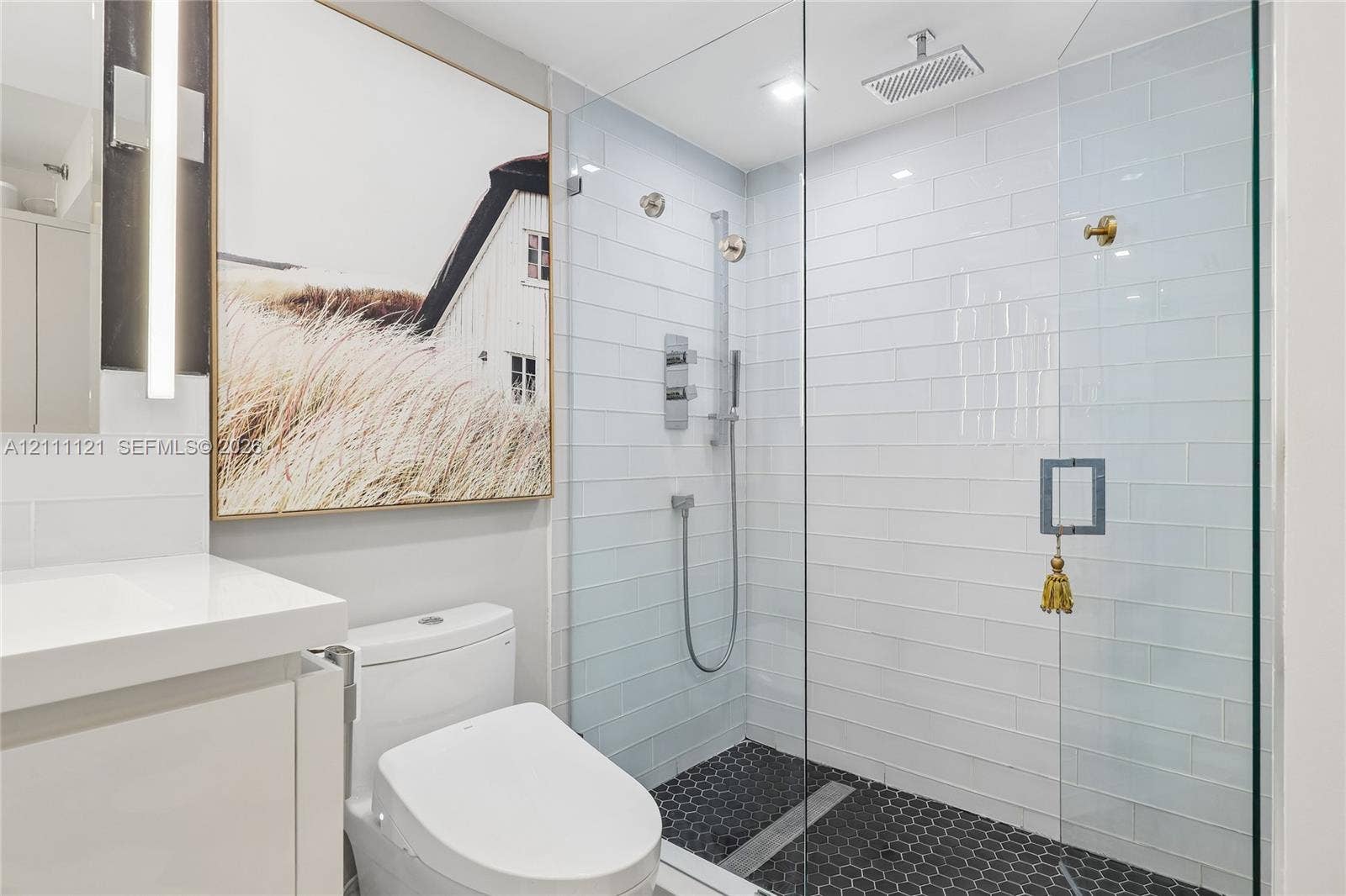 3300 NE 192nd Street, #1813, Aventura, FL 33180 Walk-in shower featuring a frameless glass enclosure, white subway tile surround, dark hexagonal floor tiling, and a rainfall showerhead
