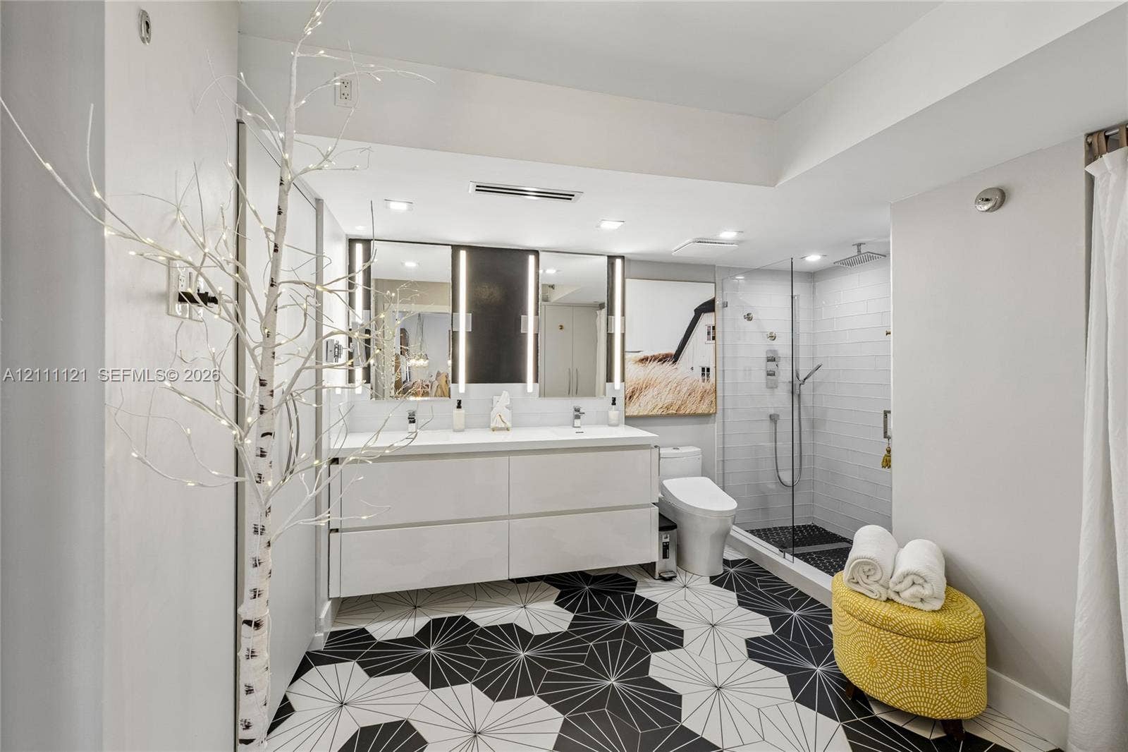 3300 NE 192nd Street, #1813, Aventura, FL 33180 Floating double vanity with integrated sinks, geometric patterned floor tiling, frameless glass-enclosed shower with wall-mounted fixtures, and dual vertical-light vanity mirrors
