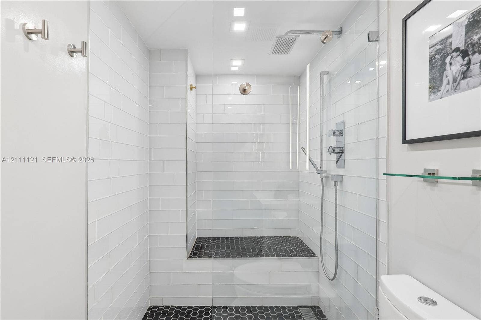 3300 NE 192nd Street, #1813, Aventura, FL 33180 Walk-in shower featuring white subway wall tile, black hexagonal floor tile, glass enclosure, rainfall shower head, and hand-held shower fixture
