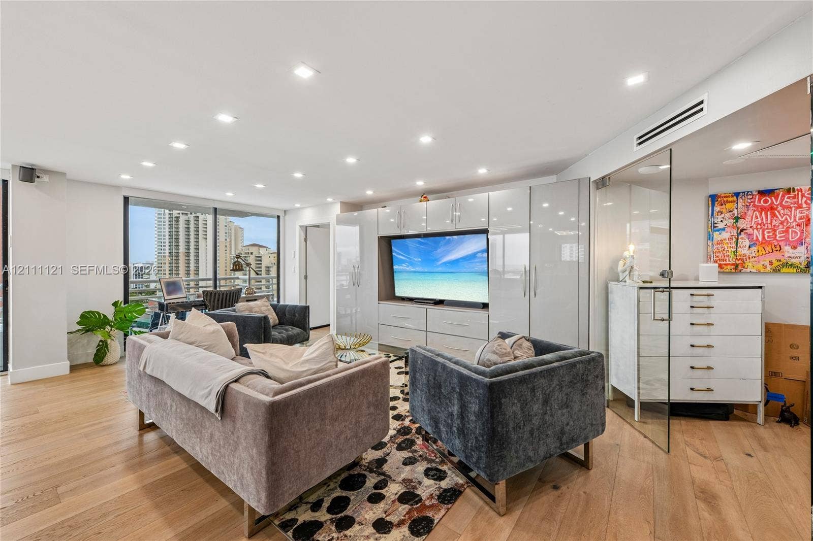 3300 NE 192nd Street, #1813, Aventura, FL 33180 Open-concept interior featuring light wood-finish flooring, recessed lighting, floor-to-ceiling glass enclosure, and high-gloss built-in cabinetry with integrated media center