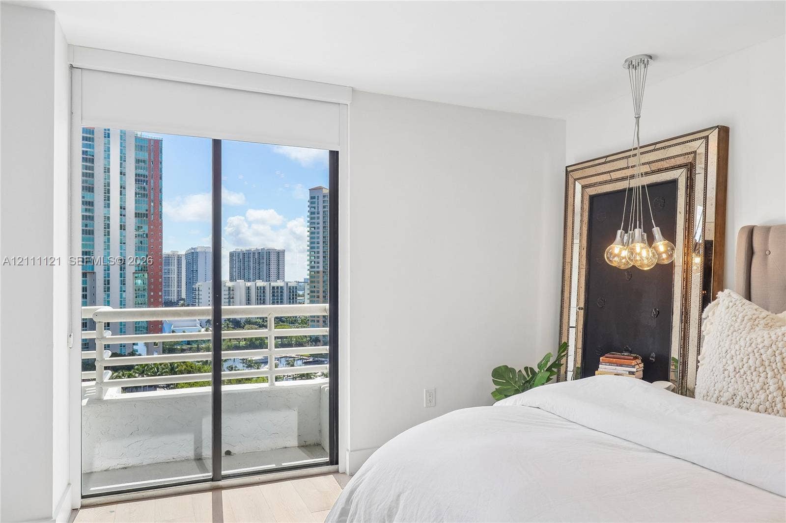 3300 NE 192nd Street, #1813, Aventura, FL 33180 Floor-to-ceiling glass sliding door, private balcony with metal railing, multi-bulb pendant lighting fixture, and wood-finish flooring