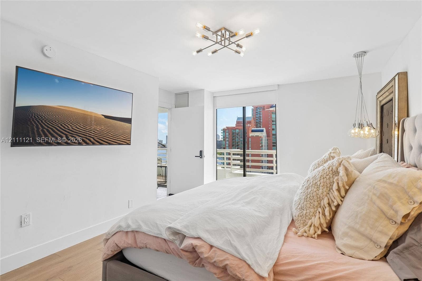 3300 NE 192nd Street, #1813, Aventura, FL 33180 Light-filled room featuring wood-finish flooring, a multi-arm modern ceiling fixture, a suspended pendant light, and a sliding glass door leading to a private balcony