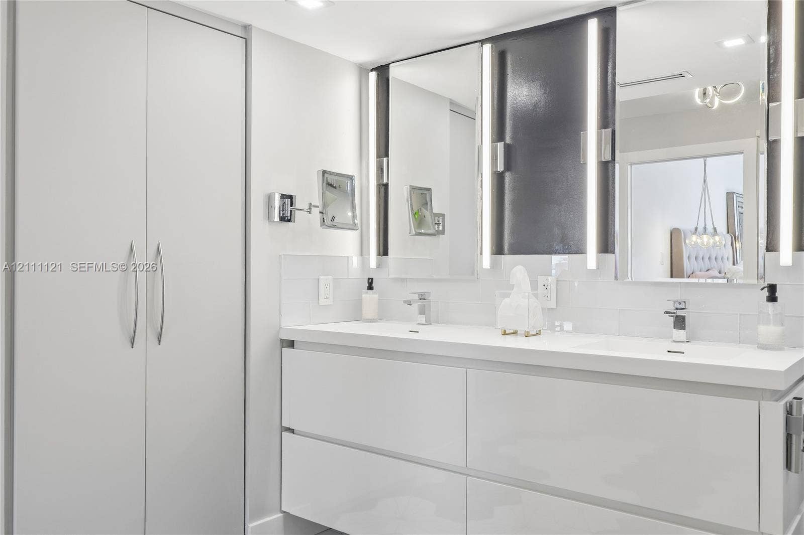3300 NE 192nd Street, #1813, Aventura, FL 33180 Dual-sink vanity featuring a white countertop, glossy white cabinetry, integrated LED mirror lighting, and a full-height built-in storage cabinet