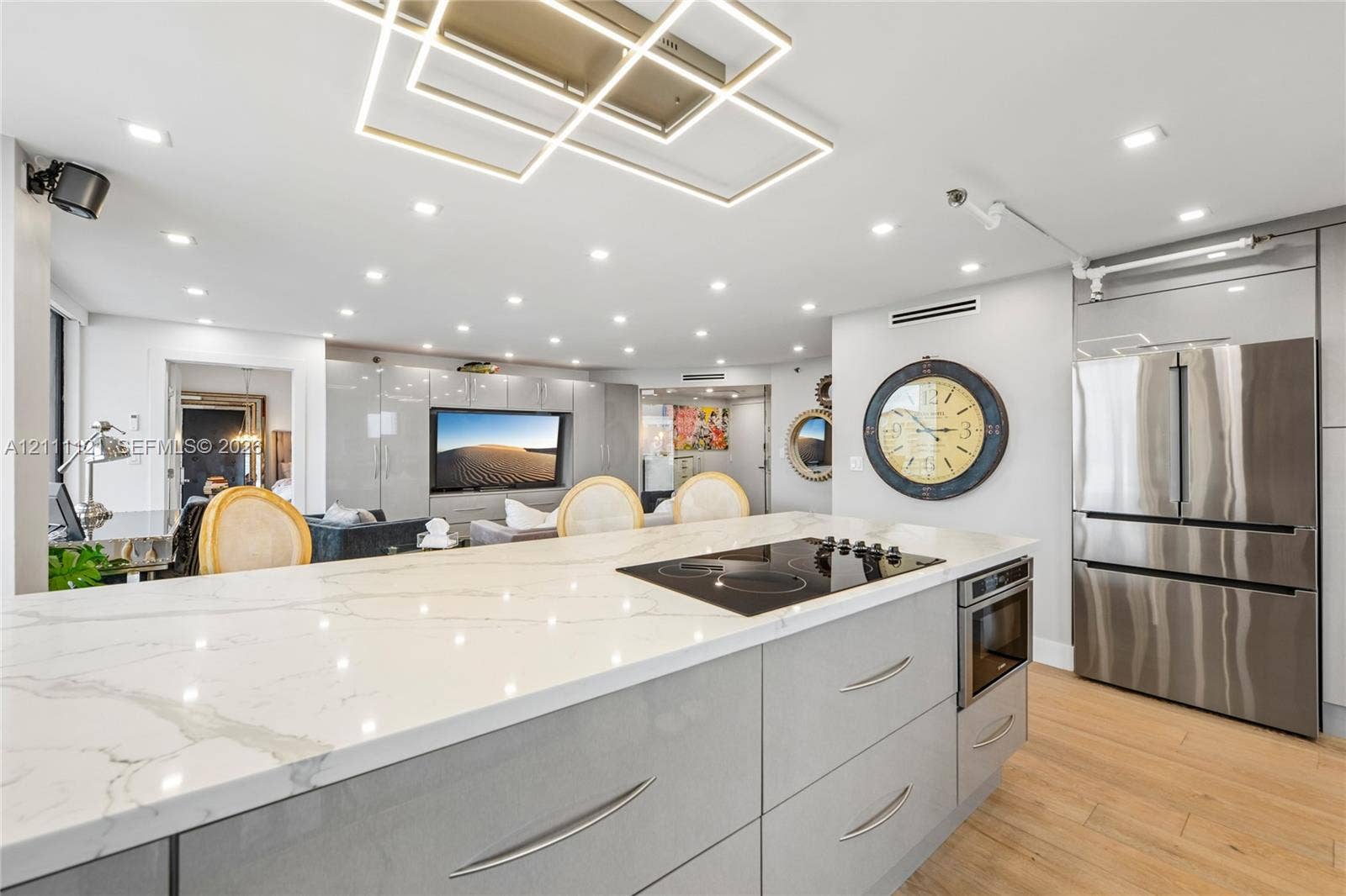 3300 NE 192nd Street, #1813, Aventura, FL 33180 Kitchen island featuring a stone-look countertop with an integrated induction cooktop, high-gloss cabinetry, wood-finish flooring, stainless steel multi-door refrigerator, and contemporary geometric recessed ceiling lighting
