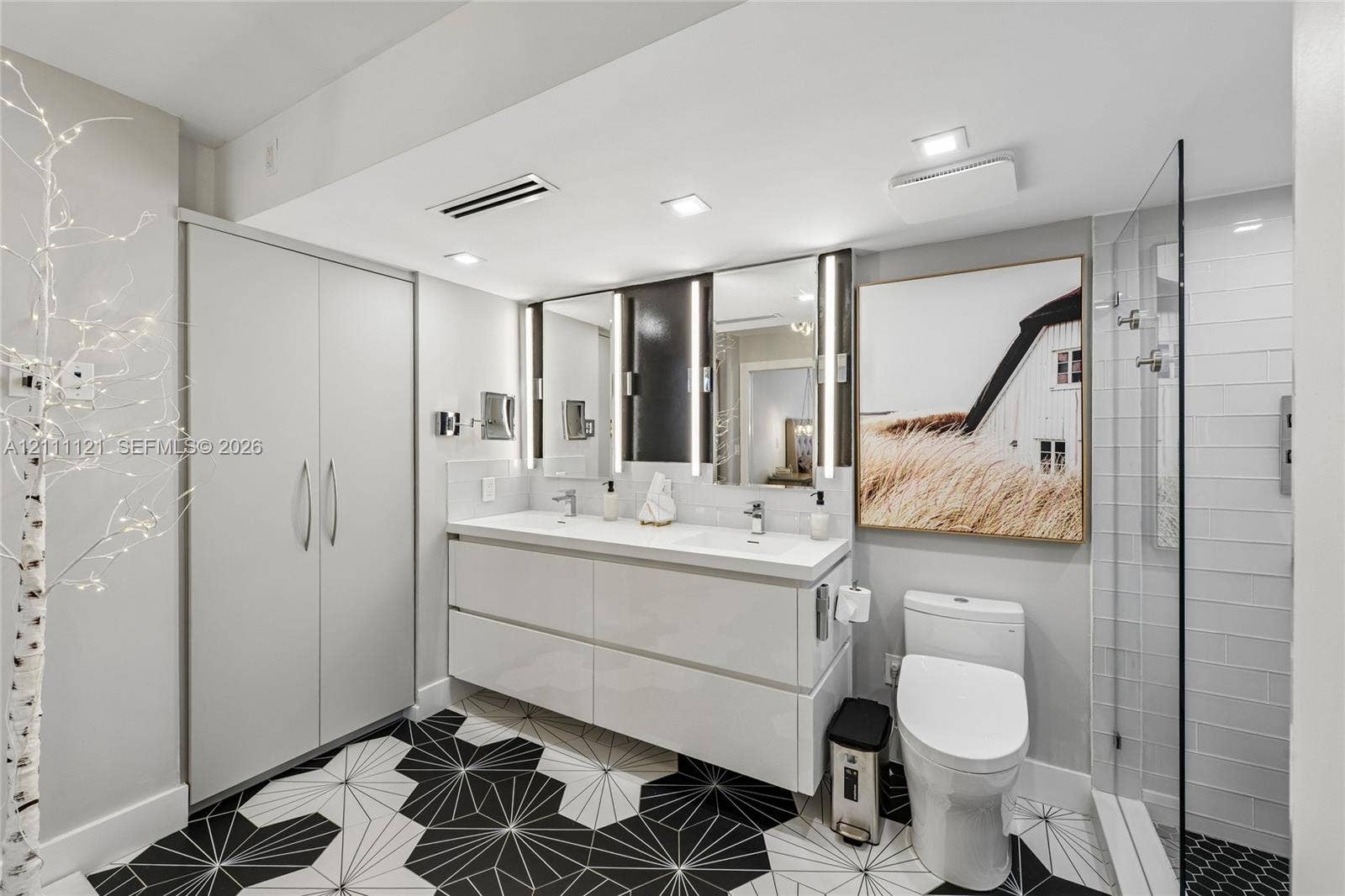 3300 NE 192nd Street, #1813, Aventura, FL 33180 Floating double vanity with integrated sinks, recessed LED vanity lighting, floor-to-ceiling cabinetry, geometric tile flooring, and glass-enclosed shower with white subway tile surround