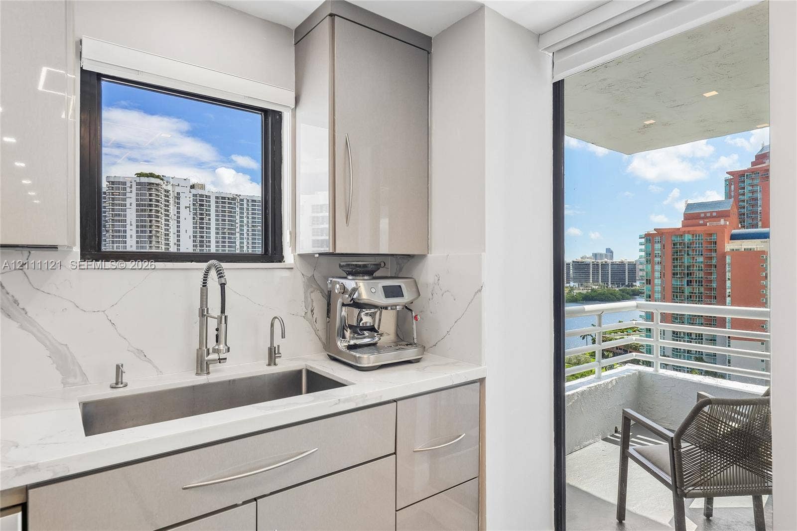 3300 NE 192nd Street, #1813, Aventura, FL 33180 Glossy cabinetry featuring integrated hardware, stone-finish backsplash, undermount stainless steel sink with high-arc pull-down faucet, and access to a private balcony