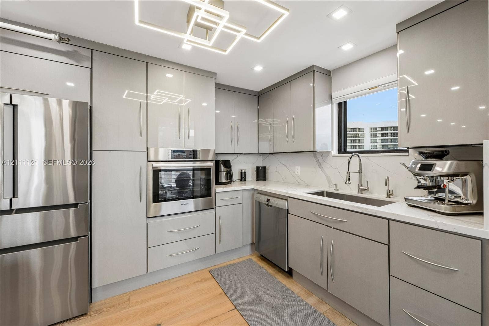 3300 NE 192nd Street, #1813, Aventura, FL 33180 Contemporary kitchen featuring high-gloss cabinetry, stone-patterned backsplash, stainless steel appliances, wood-finish flooring, and a geometric LED ceiling fixture