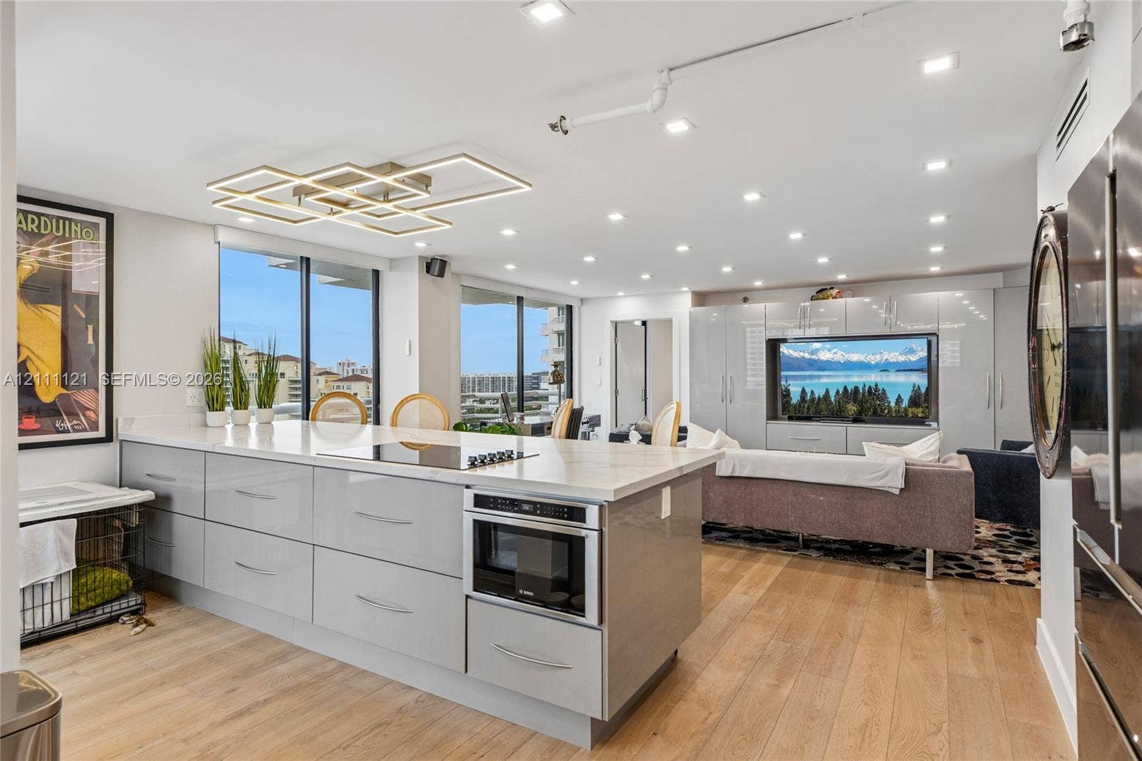 3300 NE 192nd Street, #1813, Aventura, FL 33180 Modern kitchen featuring a central island with integrated cooktop and microwave, high-gloss cabinetry, stone-surface countertops, wood-finish flooring, and geometric LED ceiling lighting
