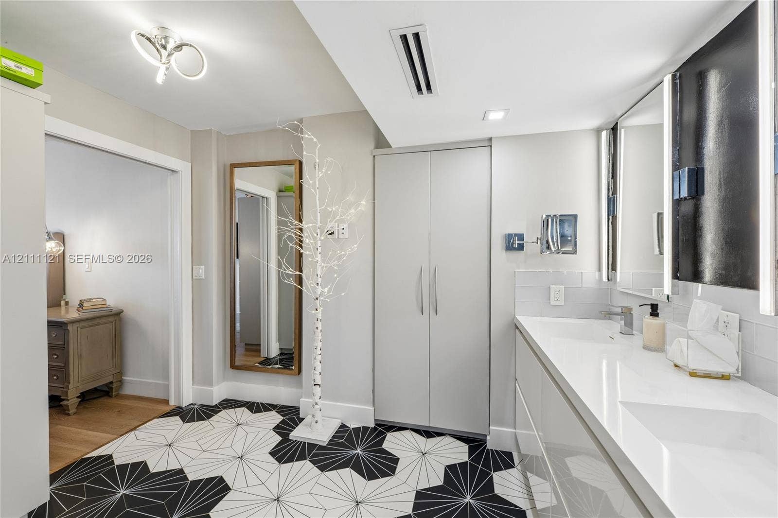 3300 NE 192nd Street, #1813, Aventura, FL 33180 Bathroom featuring geometric patterned floor tile, integrated dual-sink vanity with a solid-surface countertop, full-width mirror with integrated lighting, and floor-to-ceiling built-in cabinetry