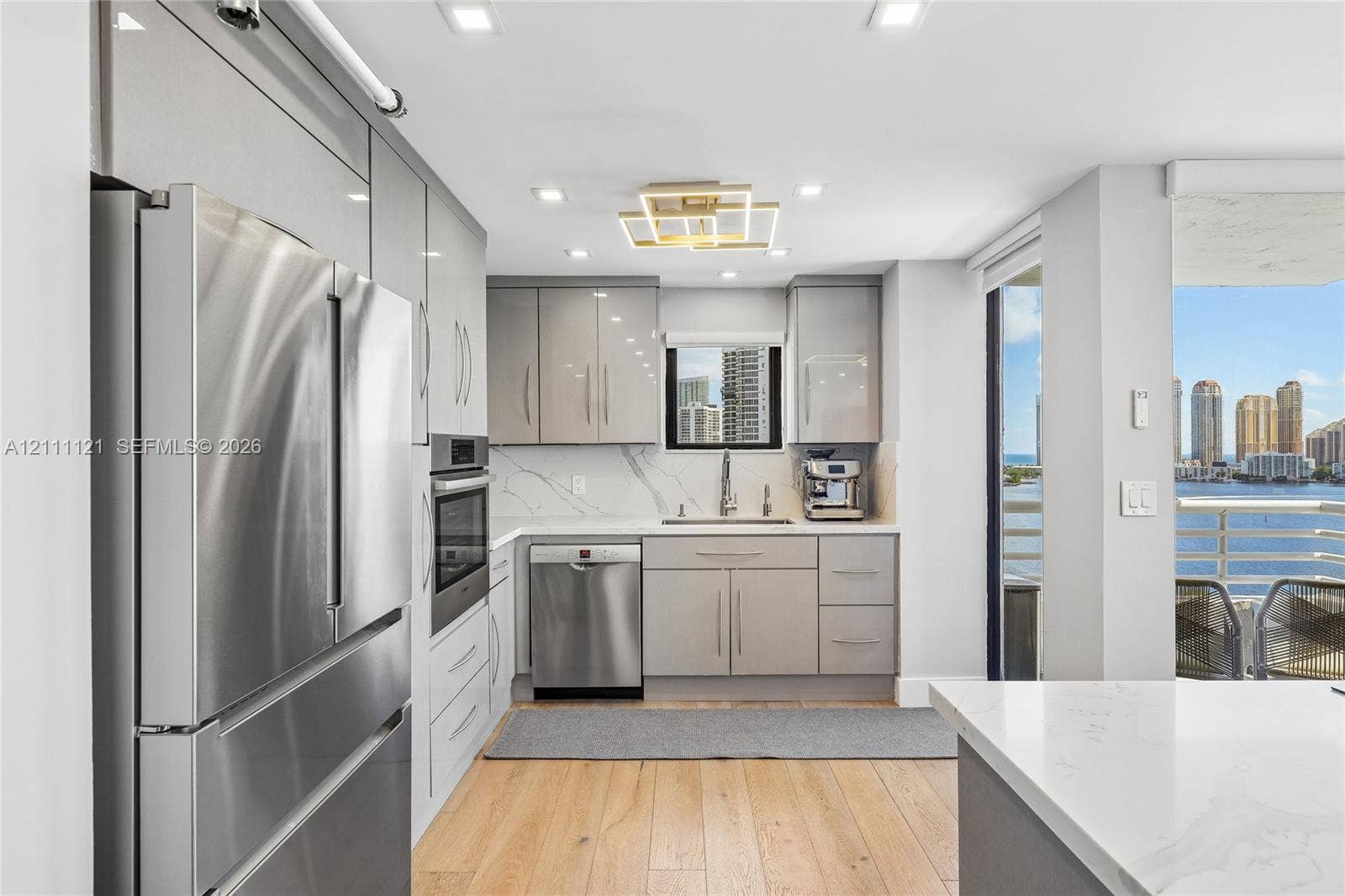 3300 NE 192nd Street, #1813, Aventura, FL 33180 Kitchen featuring high-gloss cabinetry, stone-finish countertops with matching backsplash, stainless steel appliances, recessed ceiling lighting, and wood-finish flooring