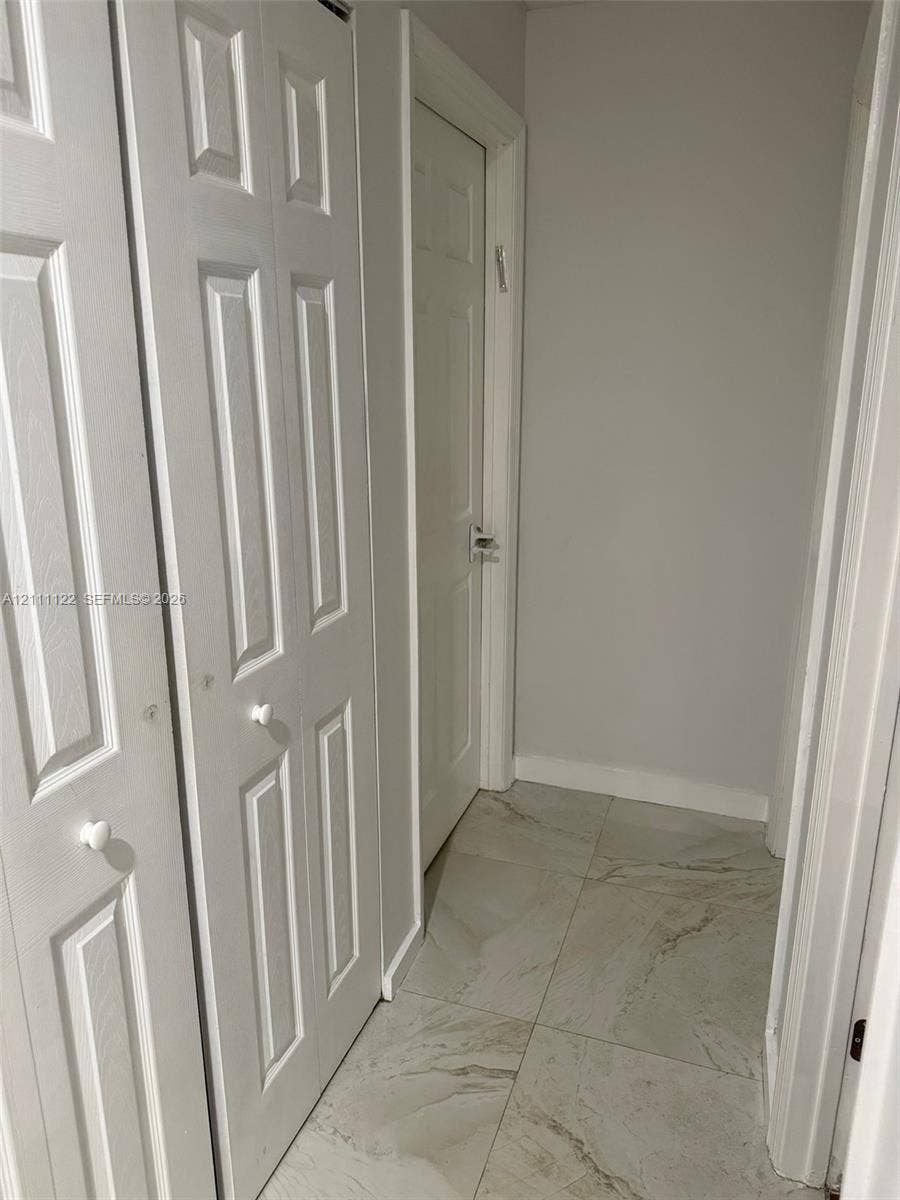 Neutral-toned interior featuring large-format tile flooring, white paneled doors, and double-door closet storage