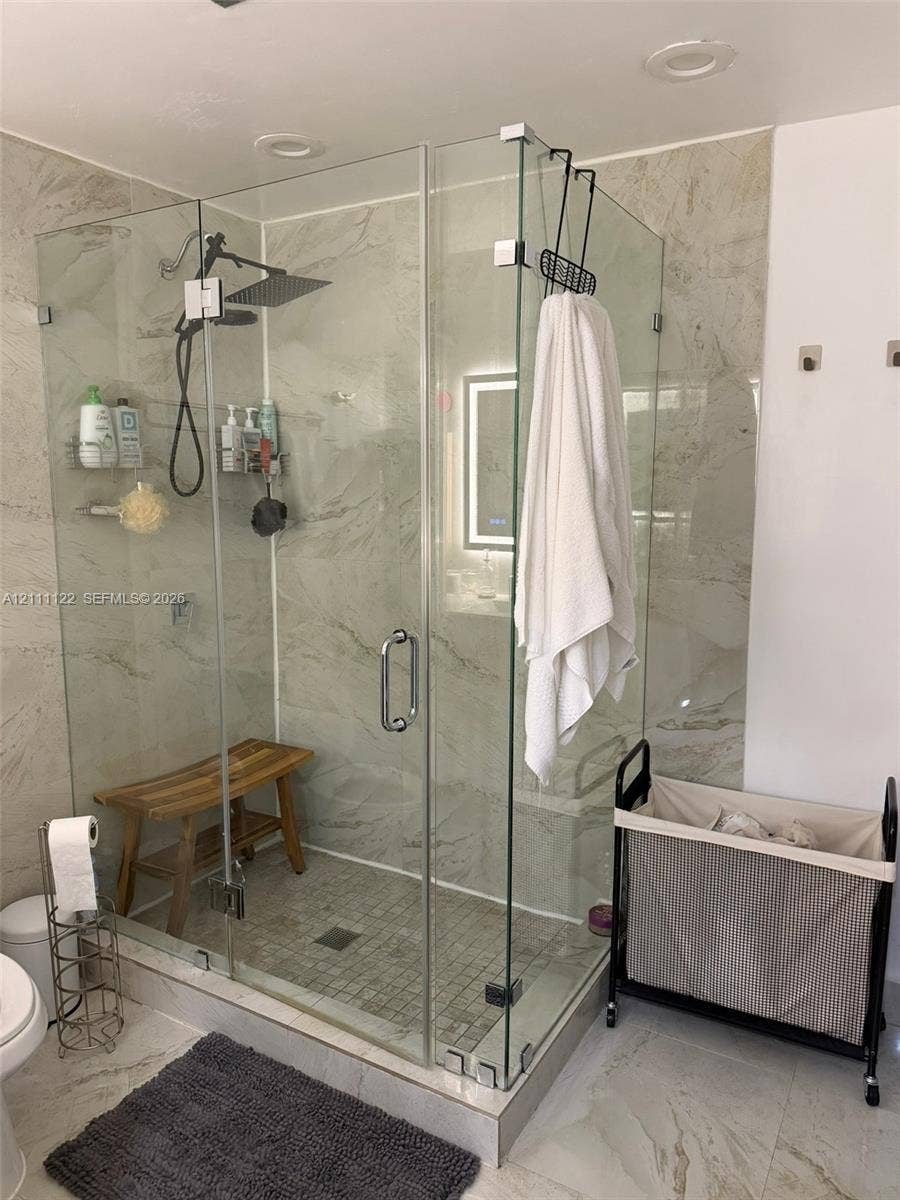 Walk-in shower featuring glass panel enclosure, large-format tile surround, rainfall shower head, and built-in bench seating