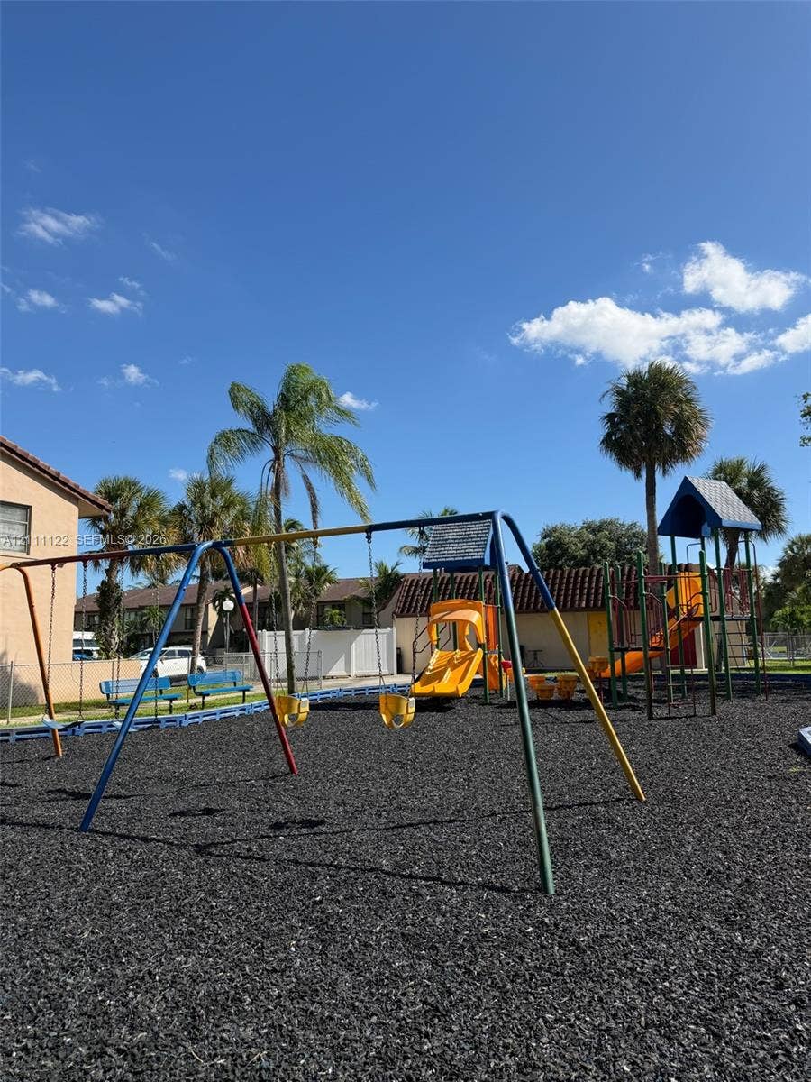 Outdoor recreational area featuring a swing set, multi-level climbing structure with slides, and rubber mulch surfacing