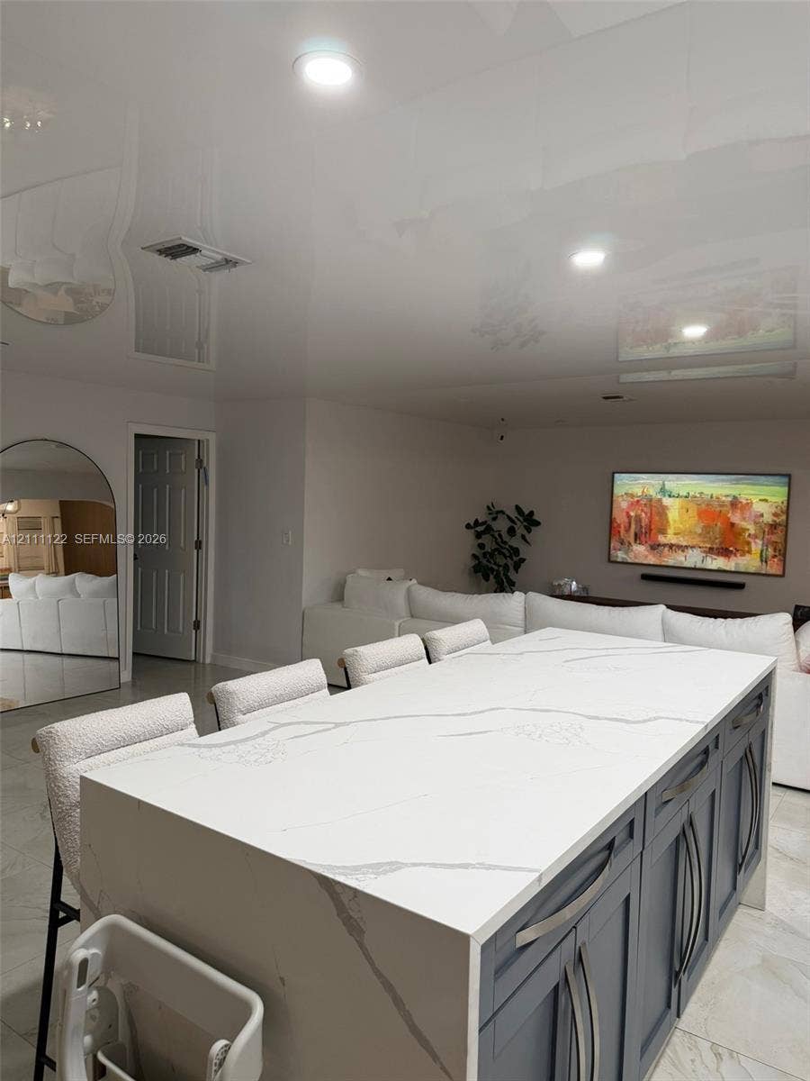Kitchen island with a white stone countertop, waterfall edge, and dark cabinetry