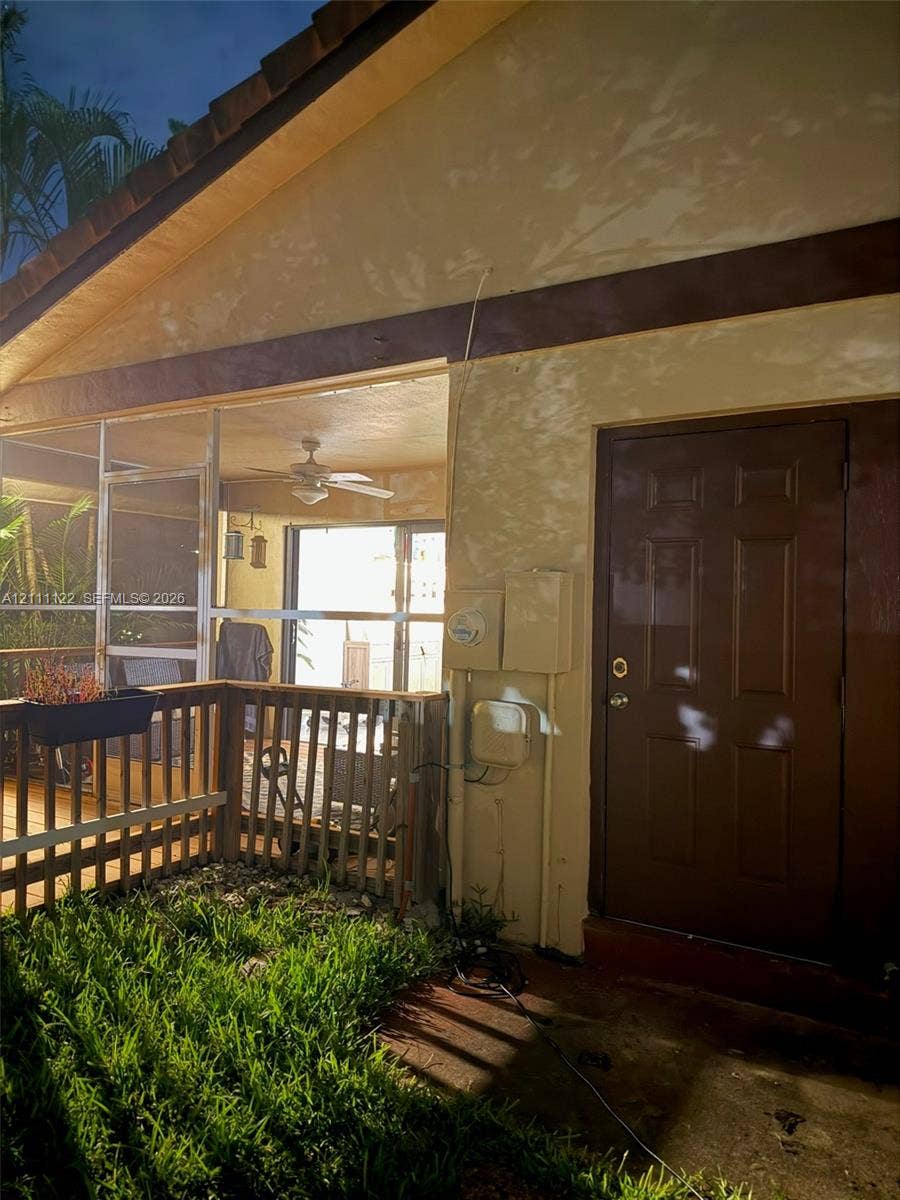 Exterior patio area featuring a screened enclosure, wood-style railing, ceiling fan, and six-panel solid door