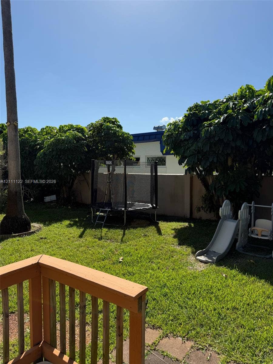 Backyard featuring a grass lawn, wooden deck, mature trees, and a perimeter masonry wall
