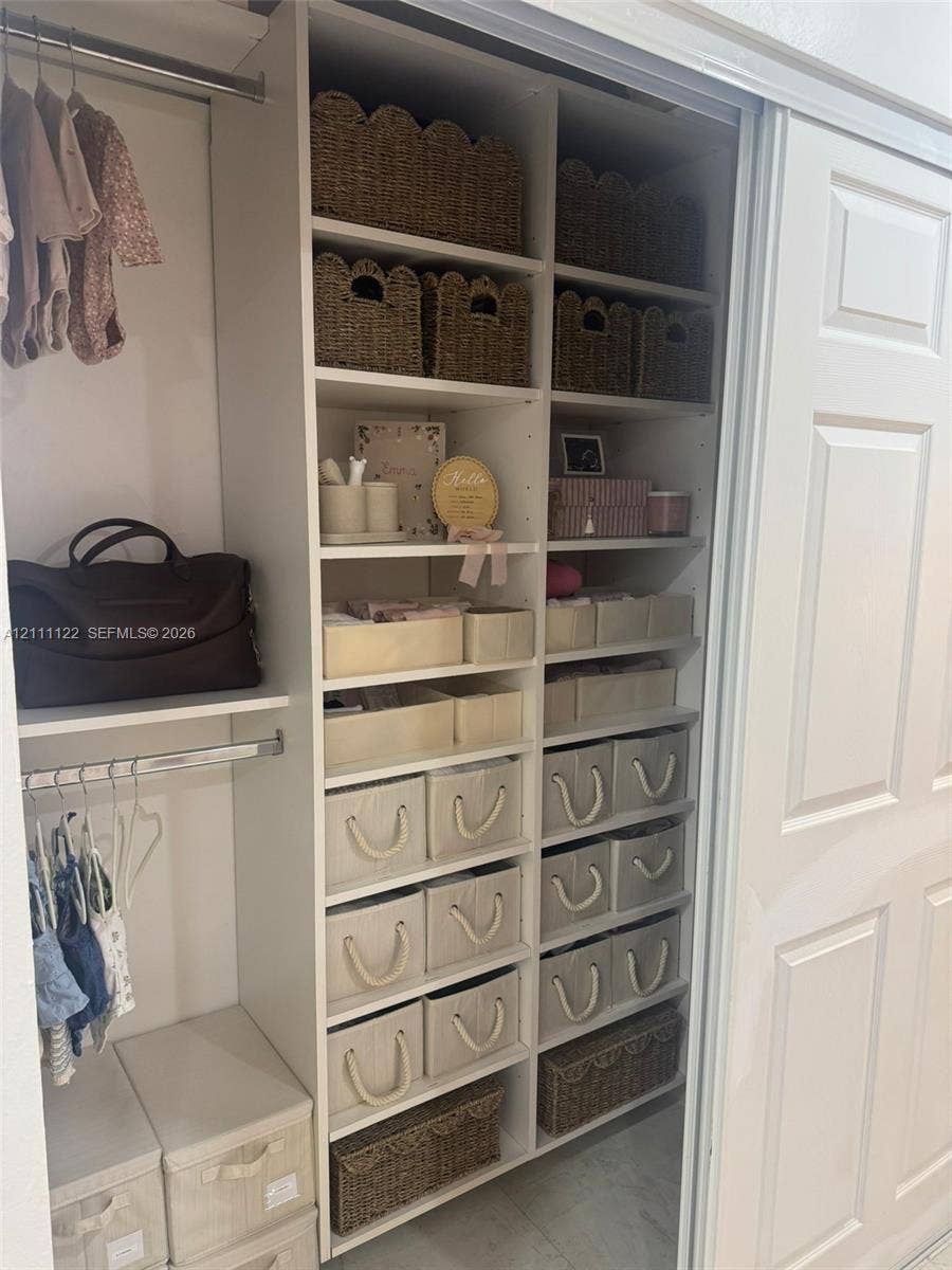 Customized built-in closet featuring white shelving, multiple storage compartments, and dual metal garment rods behind sliding panel doors