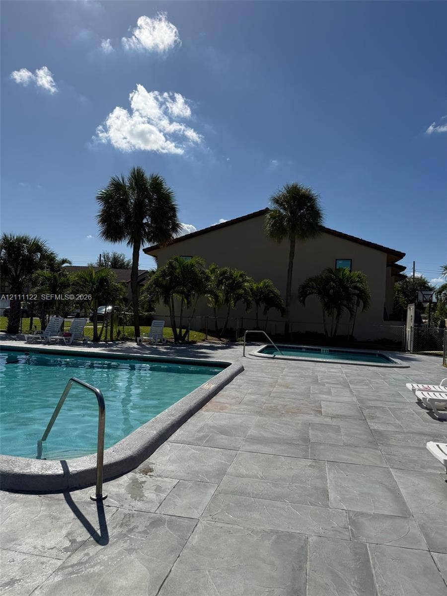 Outdoor pool and hot tub area featuring concrete paver decking, metal handrails, and mature palm trees