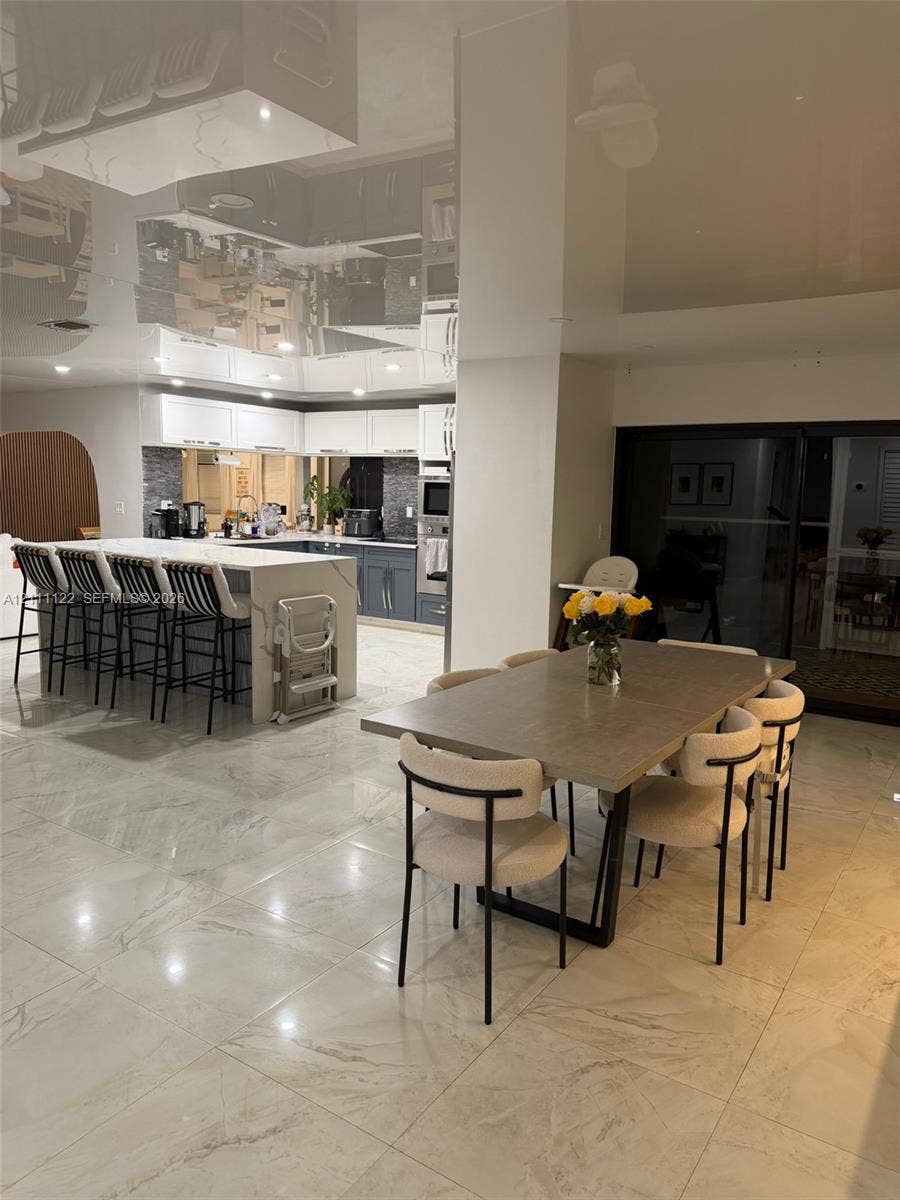 Kitchen featuring a waterfall-edge island with stone-finish countertop, dual-tone cabinetry, high-gloss ceiling finish, and polished stone-finish flooring