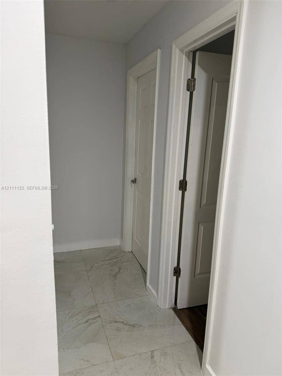 Large-format, stone-finish floor tiling with neutral veining, paired with white interior doors featuring classic panel detailing and polished metal hardware