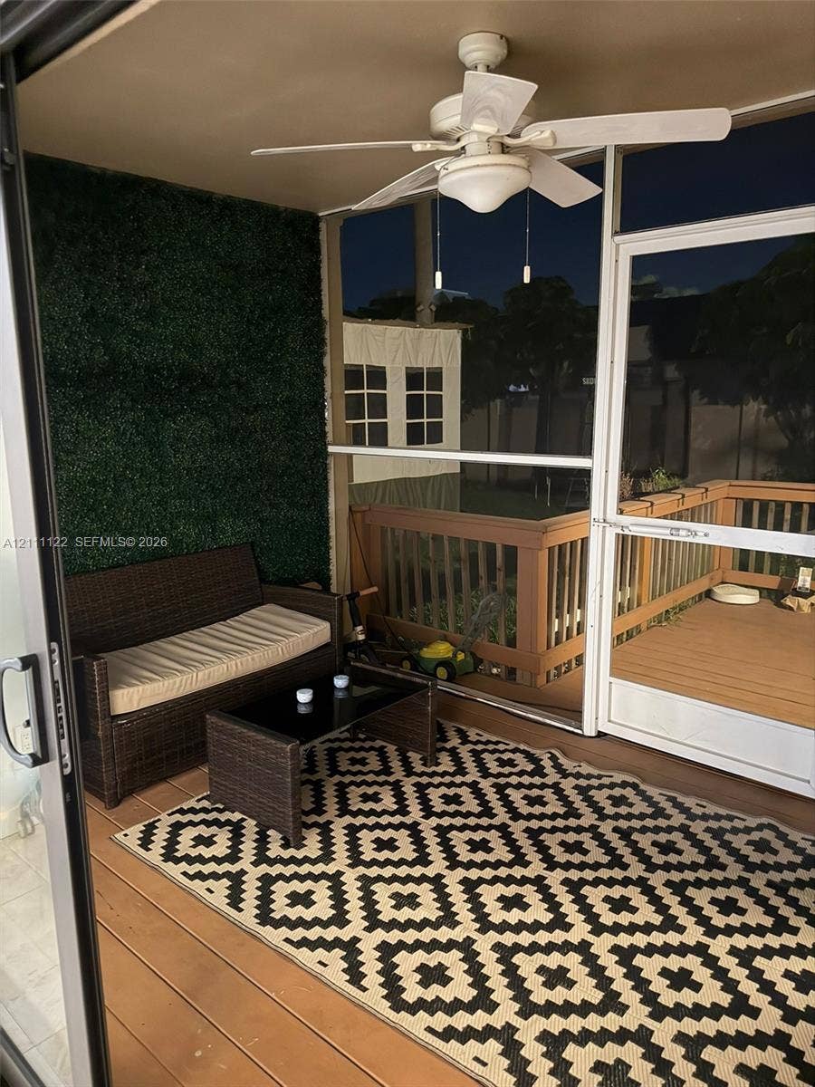 Screened-in porch featuring wood-finish flooring, a ceiling fan with integrated lighting, and a decorative faux-greenery wall panel