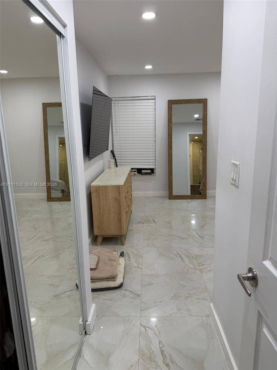 Neutral-toned large-format tile flooring, recessed ceiling lighting, sliding mirrored closet doors, and horizontal window blinds