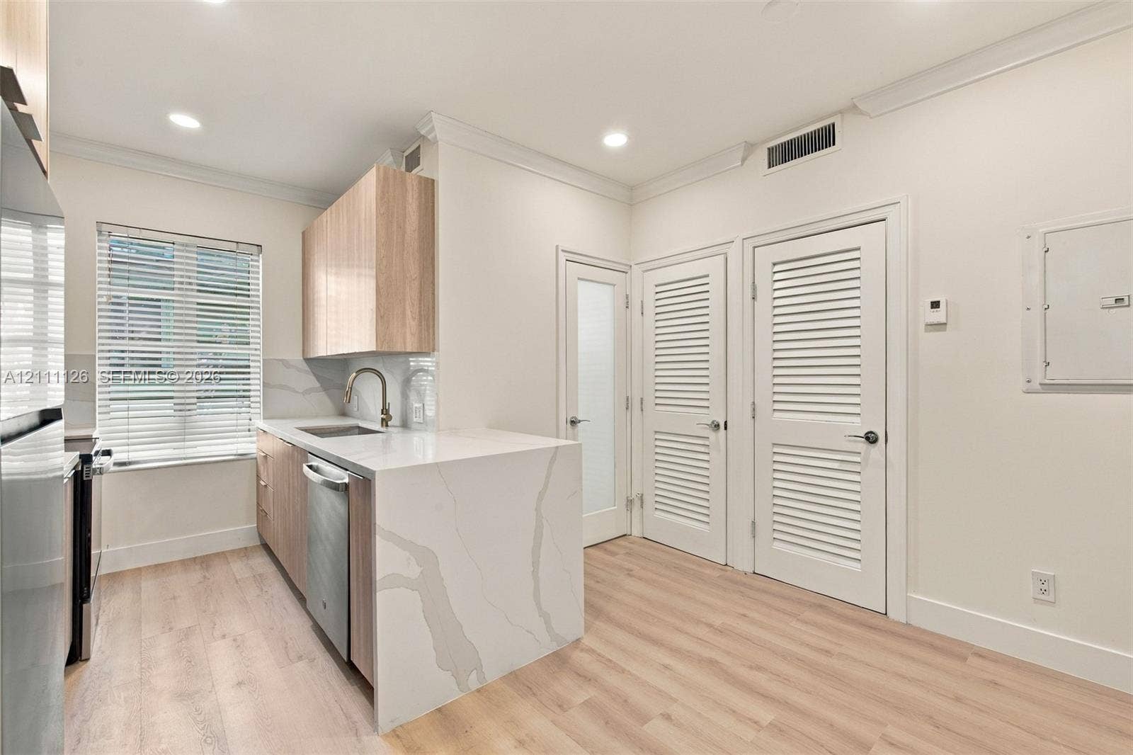 Kitchen featuring a waterfall-edge stone countertop, wood-finish cabinetry, wood-finish flooring, louvered closet doors, and recessed lighting