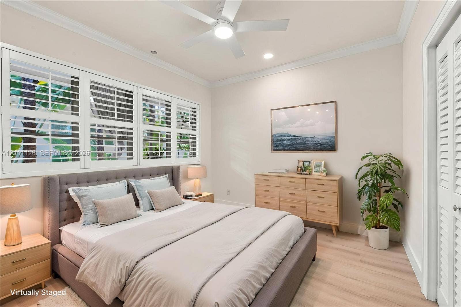 Room featuring white louvered window shutters, crown molding, wood-finish flooring, a ceiling fan with integrated lighting, and louvered closet doors