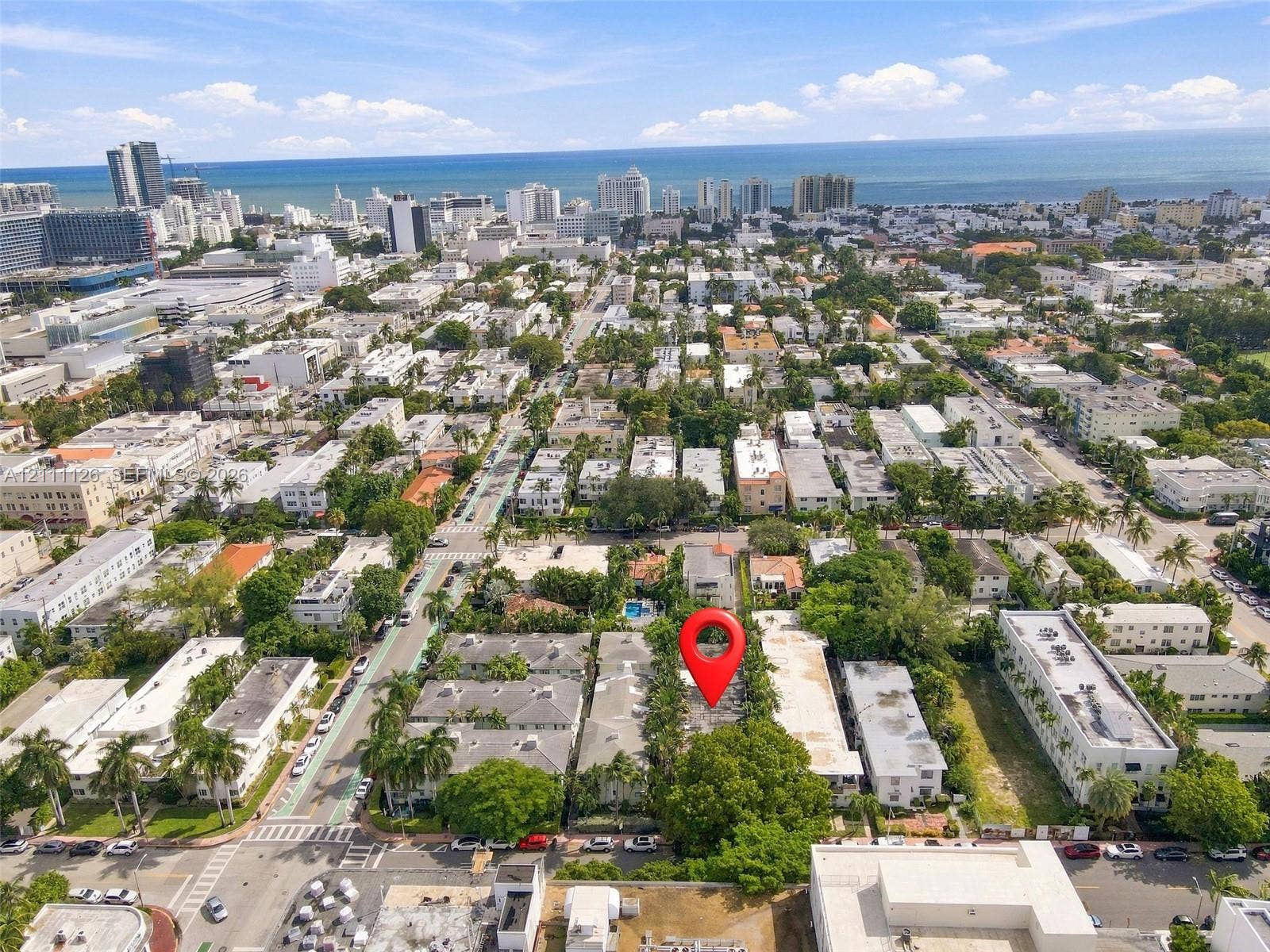 Aerial perspective of a multi-unit residential property featuring mature landscaping and a central pool area, situated within an urban coastal environment
