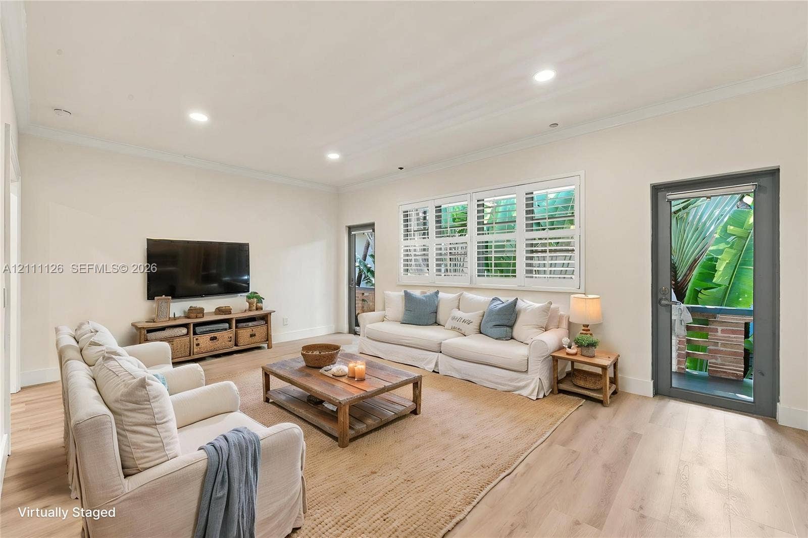 Living area featuring light-toned wood-finish flooring, recessed lighting, crown molding, multi-pane windows with plantation shutters, and two full-lite exterior doors