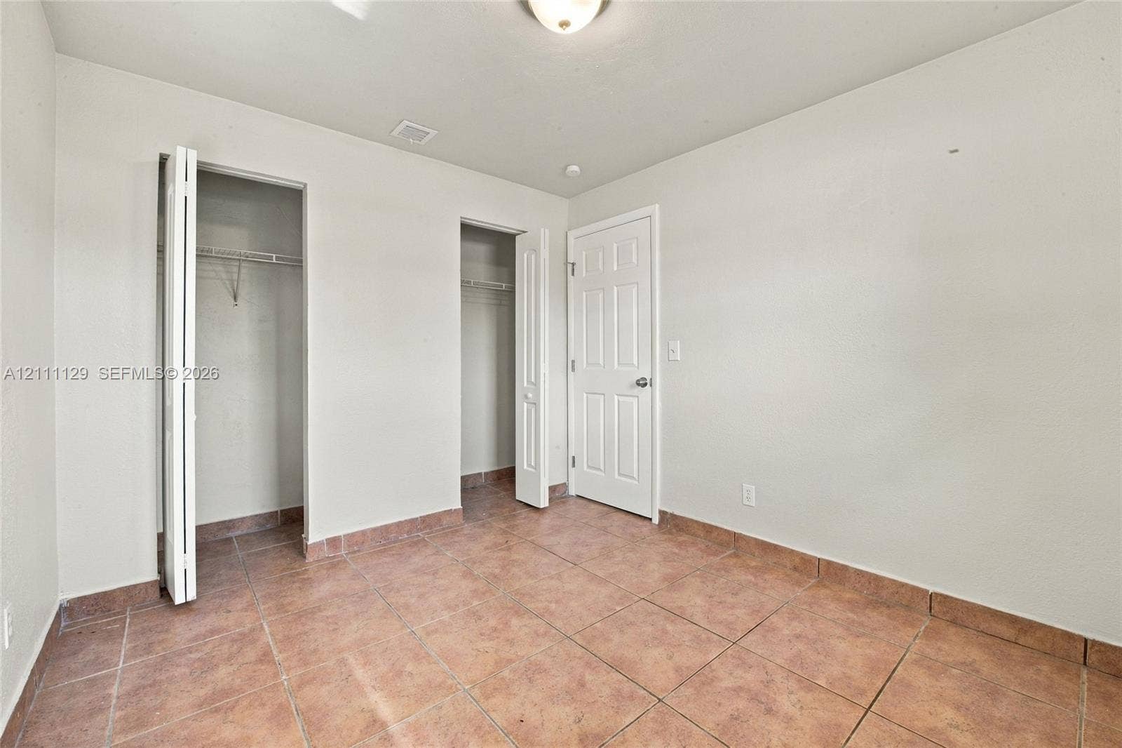 Interior room featuring large-format ceramic tile flooring, two closets with bi-fold doors, and a paneled interior door with a brushed-metal knob