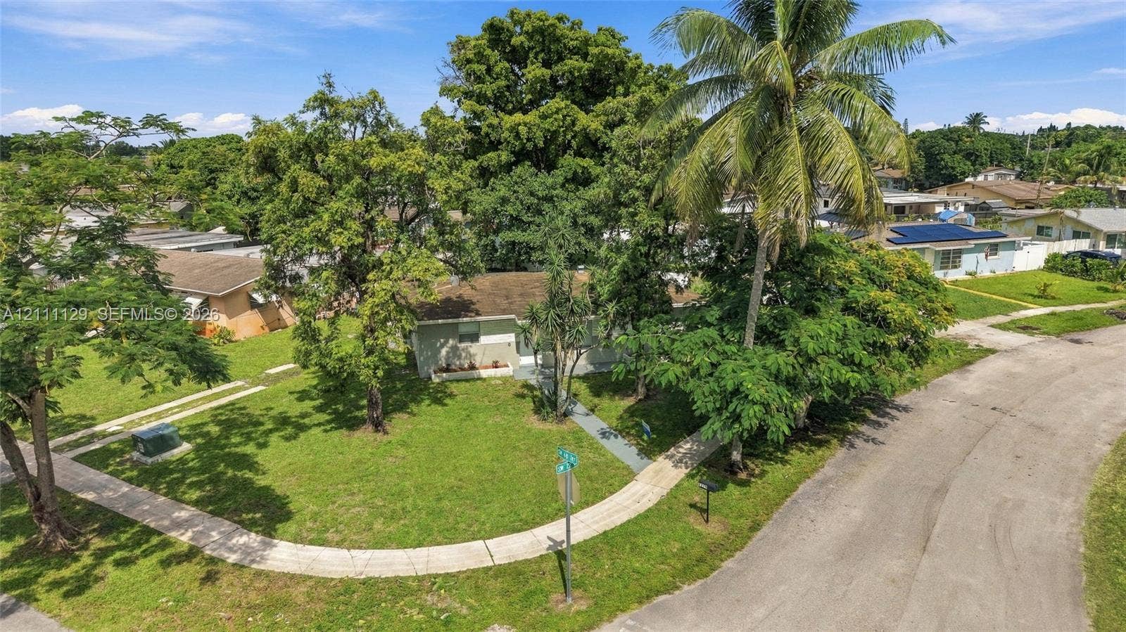 Corner lot exterior featuring established mature trees, manicured lawn, and concrete walkways