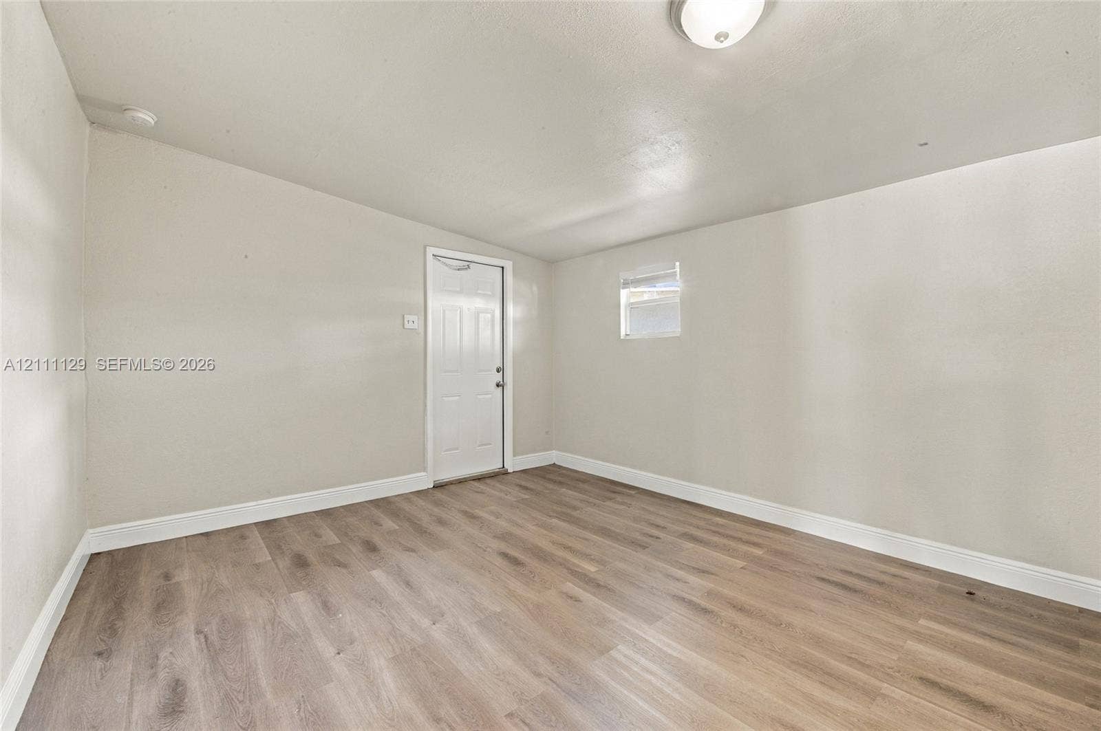 Interior space featuring wood-finish flooring, neutral wall tones, a six-panel door, and a flush-mount ceiling light fixture