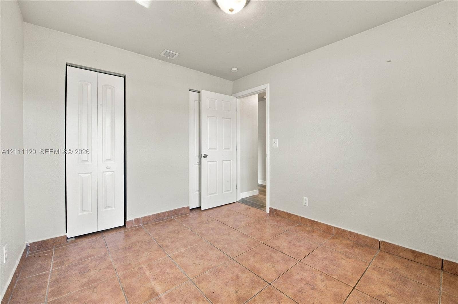 Interior space featuring neutral-toned walls, tile flooring, a six-panel swing door, and bi-fold closet doors