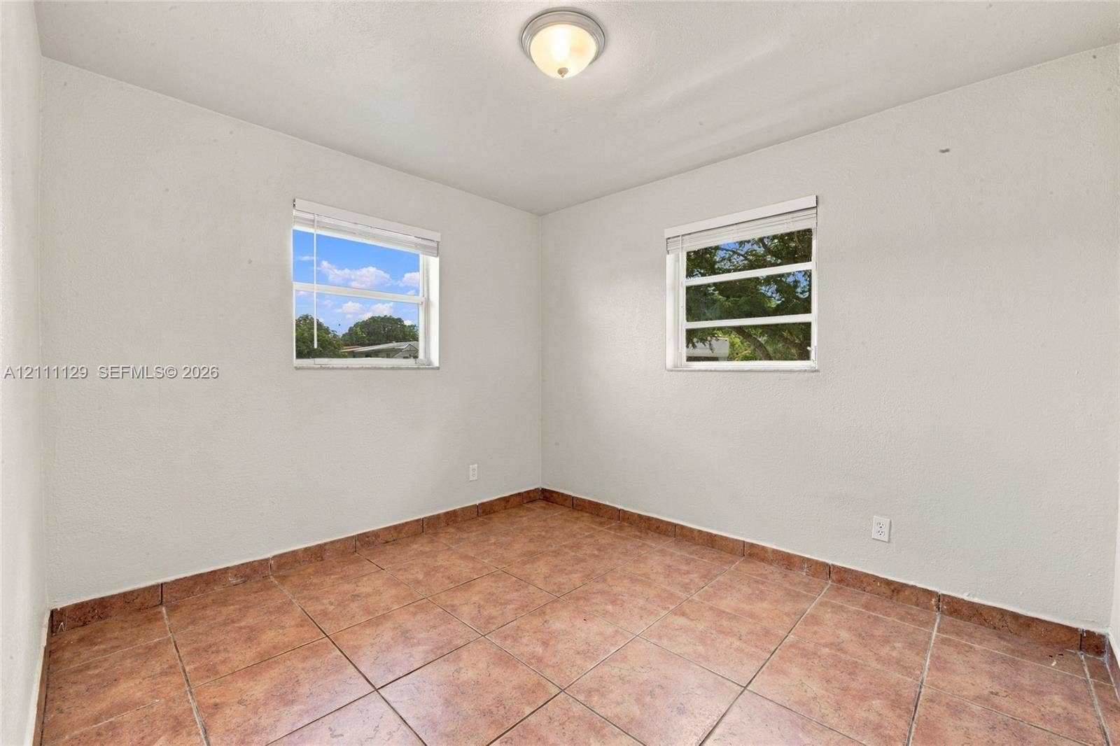 Neutral-toned room featuring tiled flooring, two double-hung windows, and a flush-mount ceiling light fixture