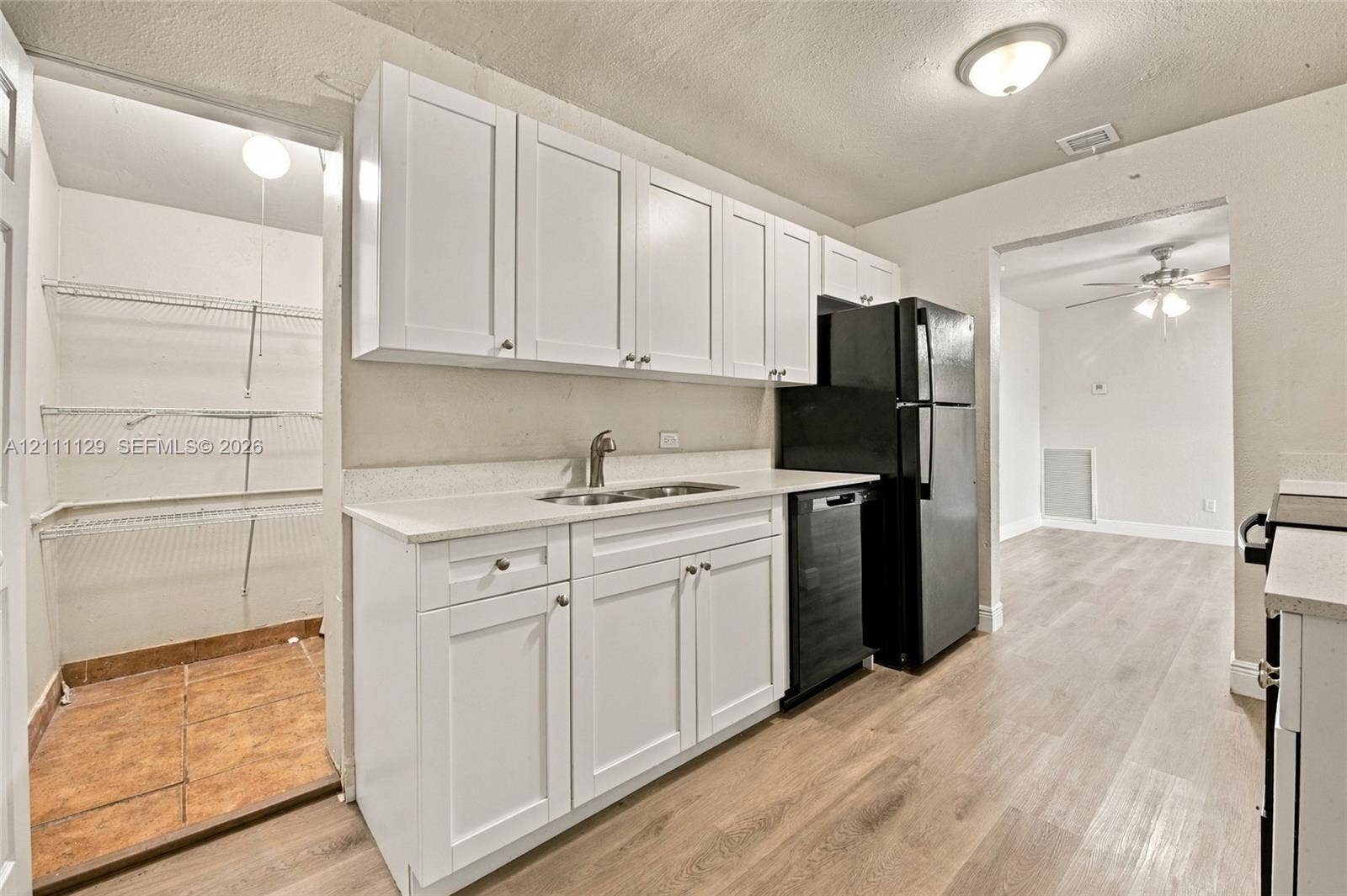 Kitchen featuring white shaker-style cabinetry, solid-surface countertops, dual-basin stainless steel sink, black dishwasher, and wood-finish flooring