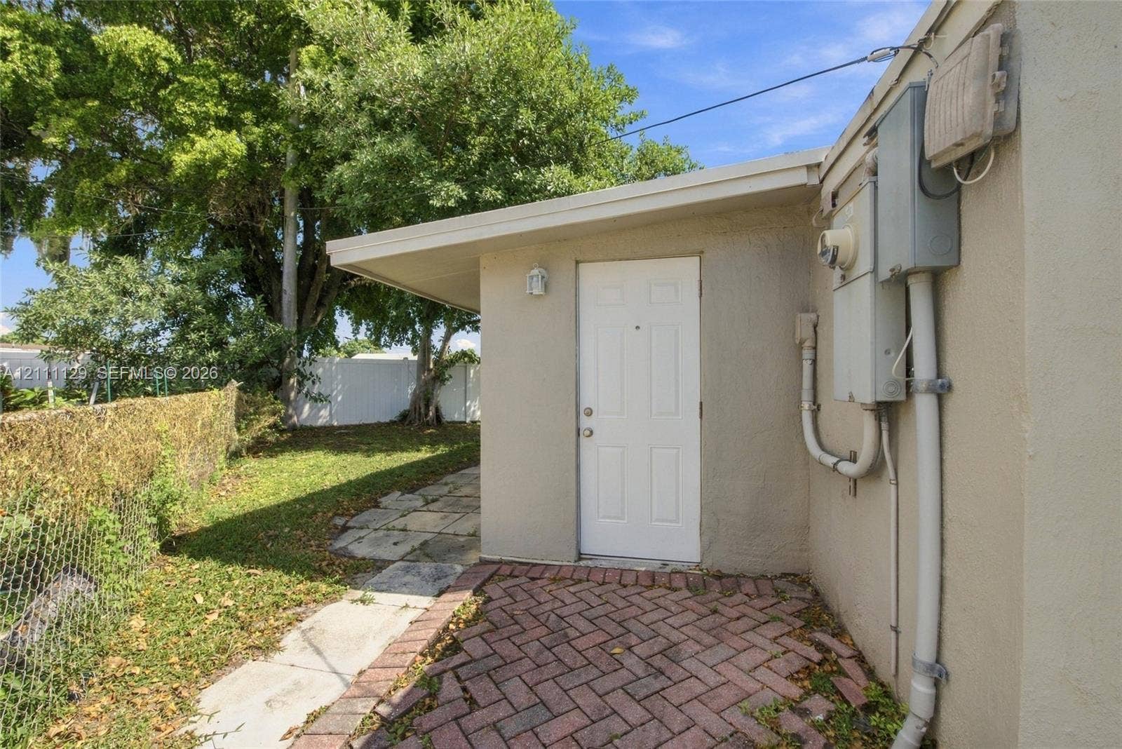 Exterior entry featuring a white door, herringbone-pattern brick patio, and a stone walkway