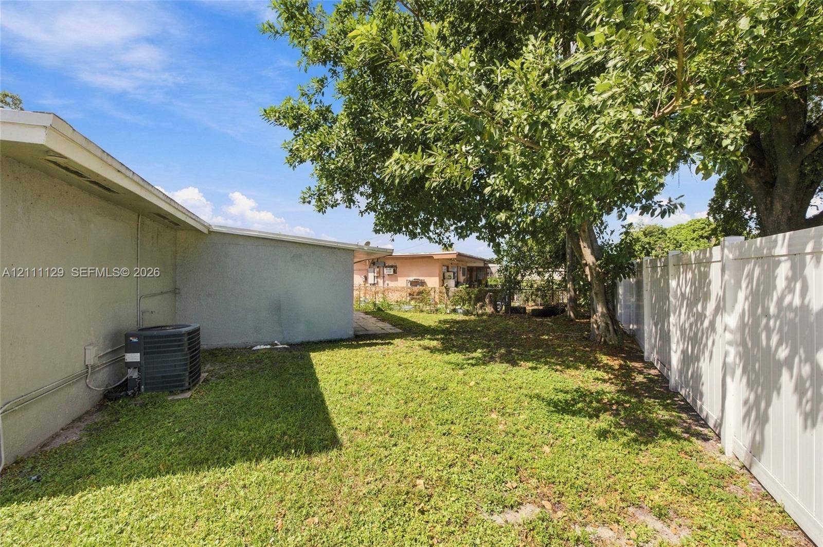 Backyard area featuring a vinyl privacy fence, mature shade trees, and a grass lawn